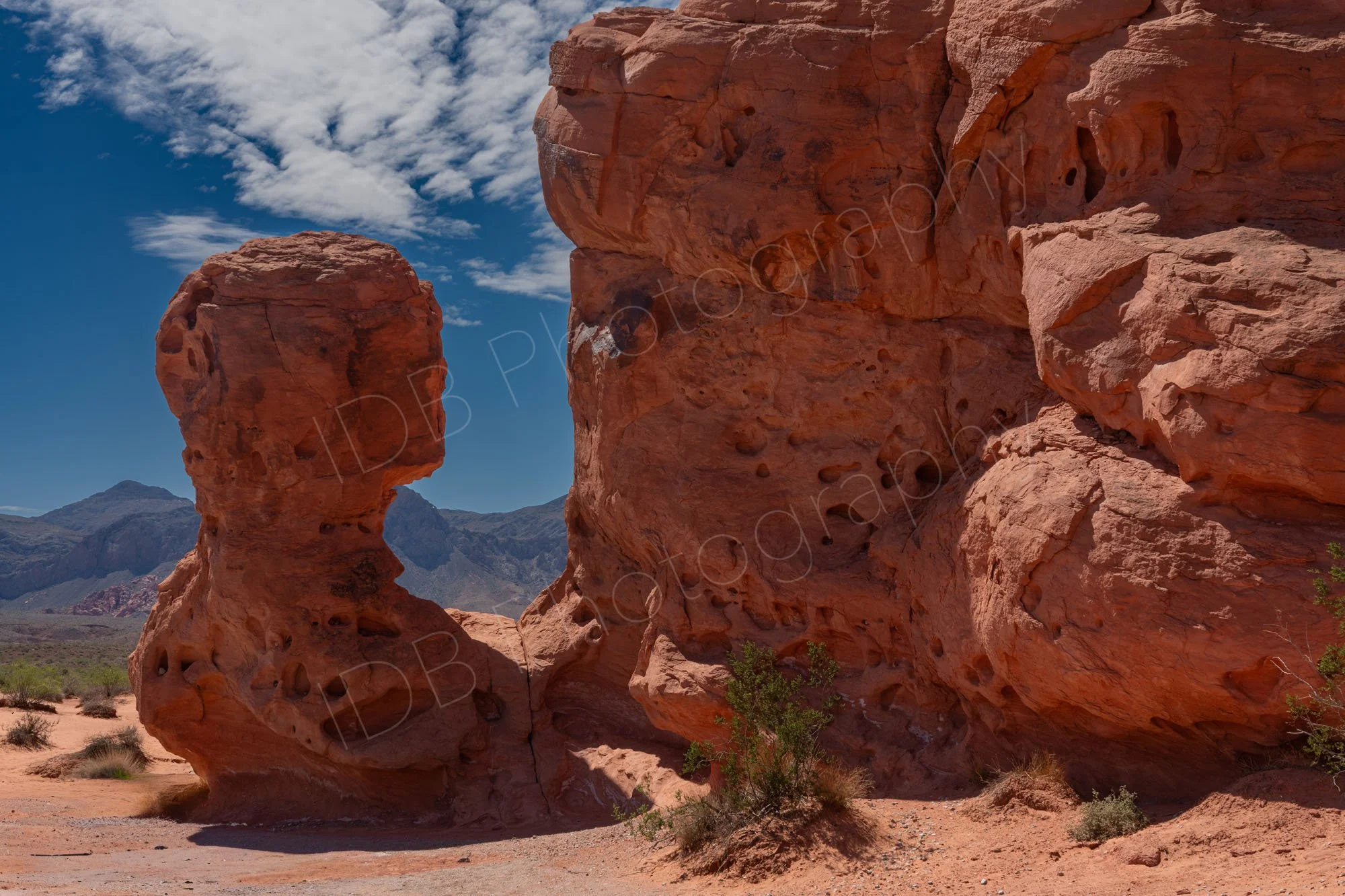 An unusual red "head and shoulders" rock formation with larger vertical red rocks and a cloudy blue sky in Valley of Fire, Nevada.