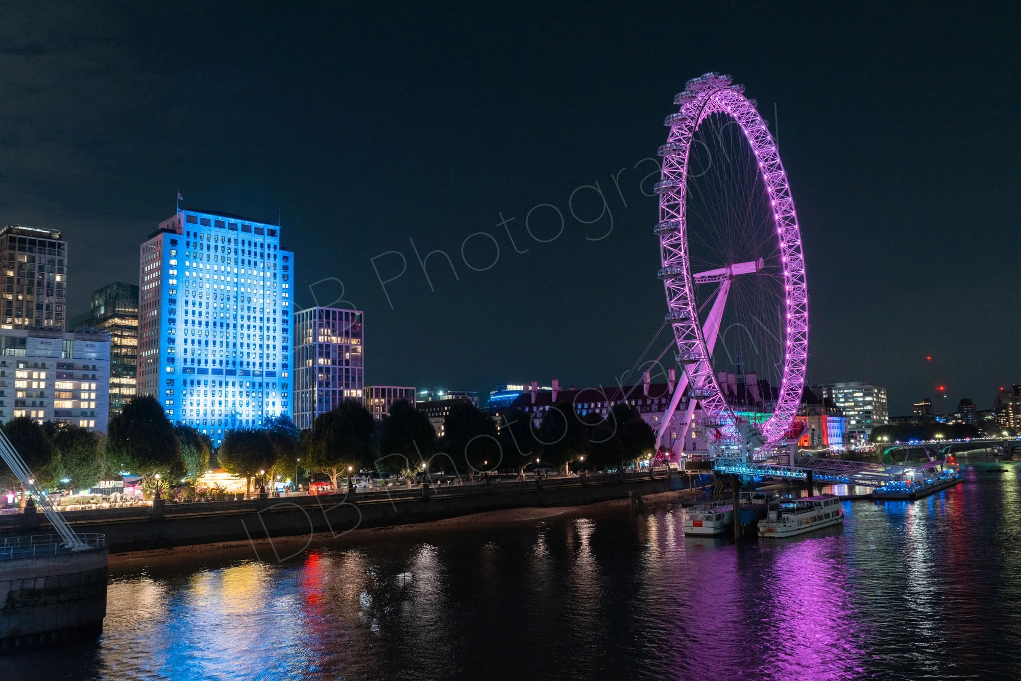 A night view from Waterloo Bridge across the Thames towards the pink lit London Eye, and the light blue Shell Centre, both reflecting nicely in the water.