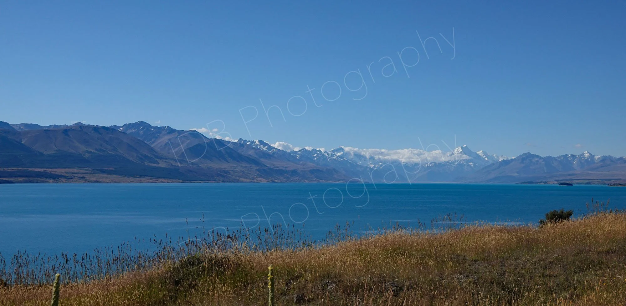 Blue waters of Lake Pukaki , Canterbury, New Zealand with Mount Cook in the distance and lovely blue sky.