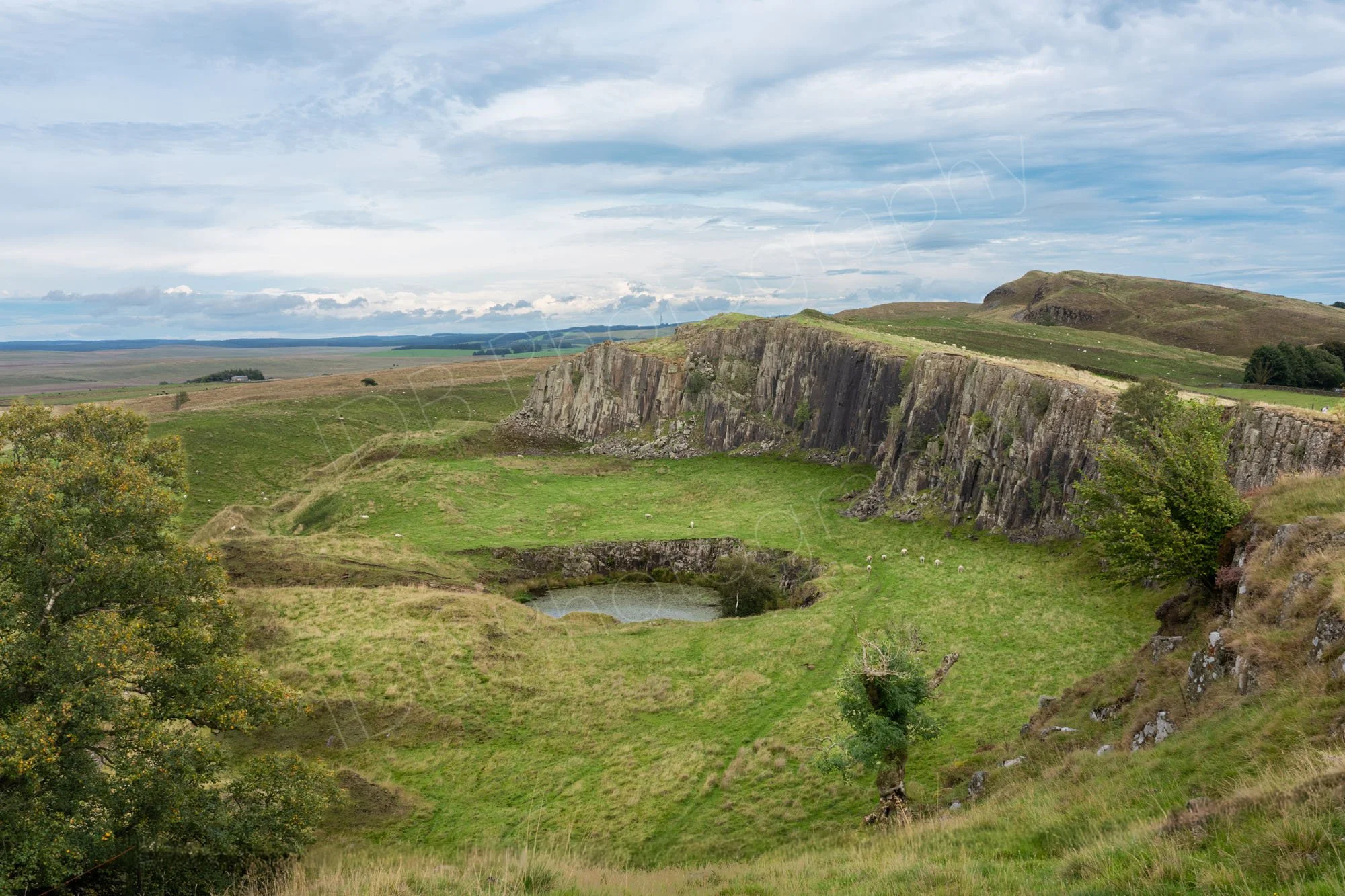 Walltown crags, Hadrian's wall, fields, small pond and greyish blue cloudy sky.