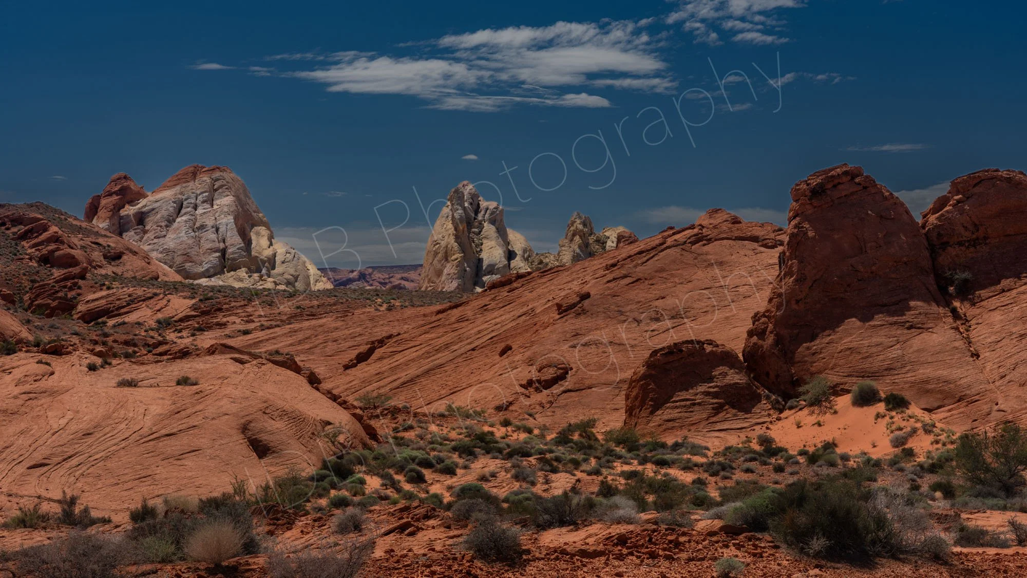 A mainly red rock with buff landscape, scrubby desert and cloudy blue sky background in Valley of Fire, State Park, Nevada.