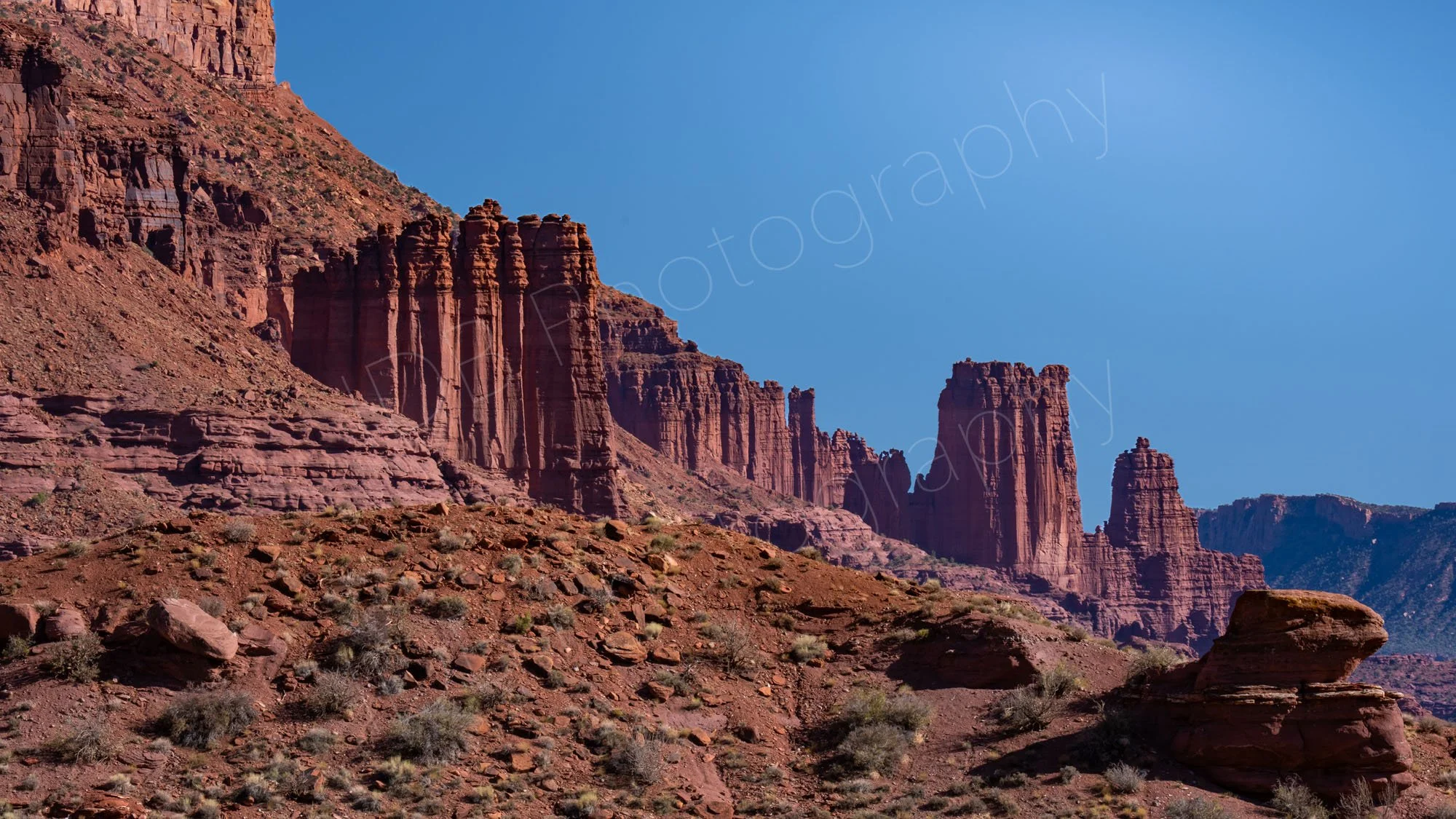 A close up view of the dramatic red sandstone pillars of the Fisher Towers near Moab, Utah, blue sky background.