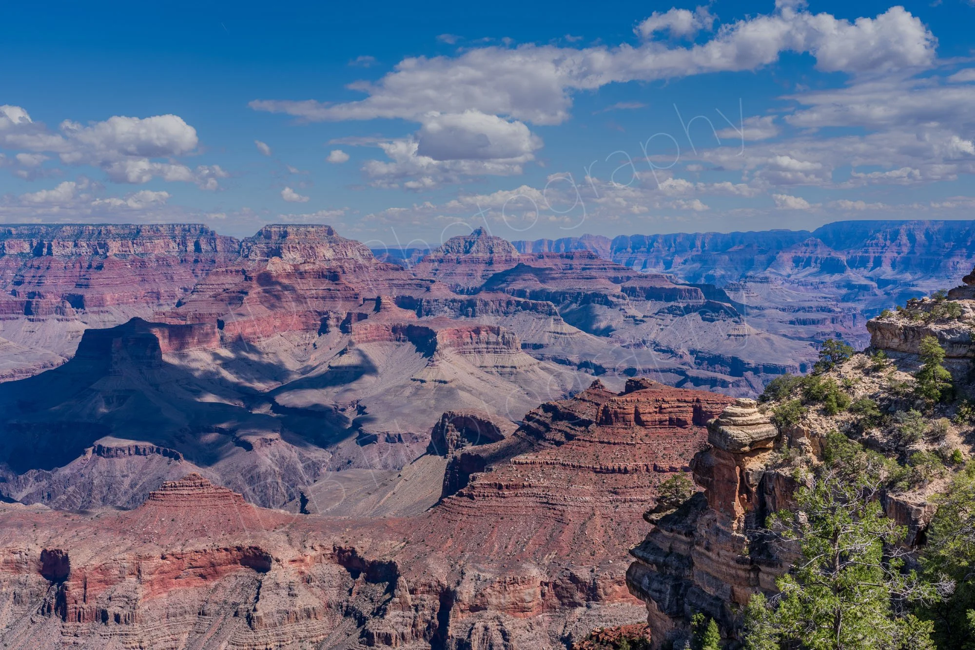 A panoramic view of the layered red rock cliffs and deep gorges of the Grand Canyon South Rim in Arizona, USA with a cloudy blue sky.