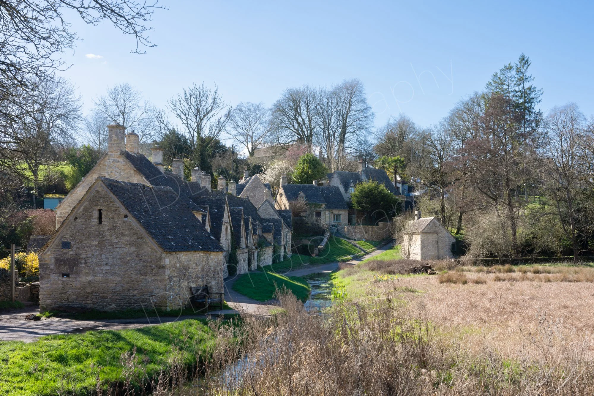 Arlington Row, a famous street of old stone cottages in the rural village of Bibury, Gloucestershire, pale blue sky.