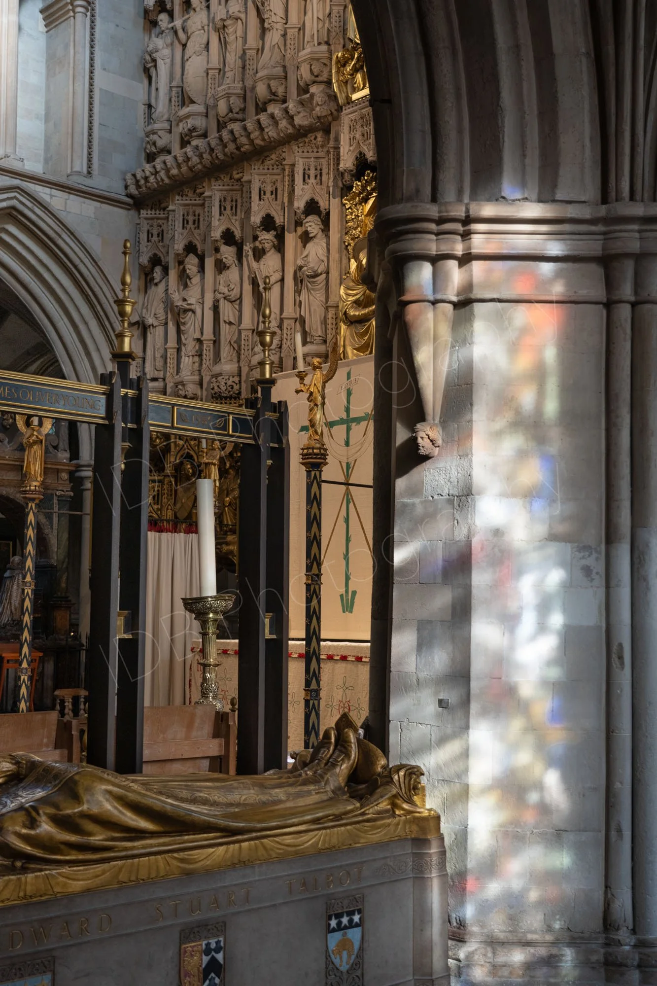 Beautiful light from stained glass windows onto a pillar at Southwalk Cathedral. The legs of the bronze effigy of Bishop Talbot can be seen along with a number of carved stone figures.