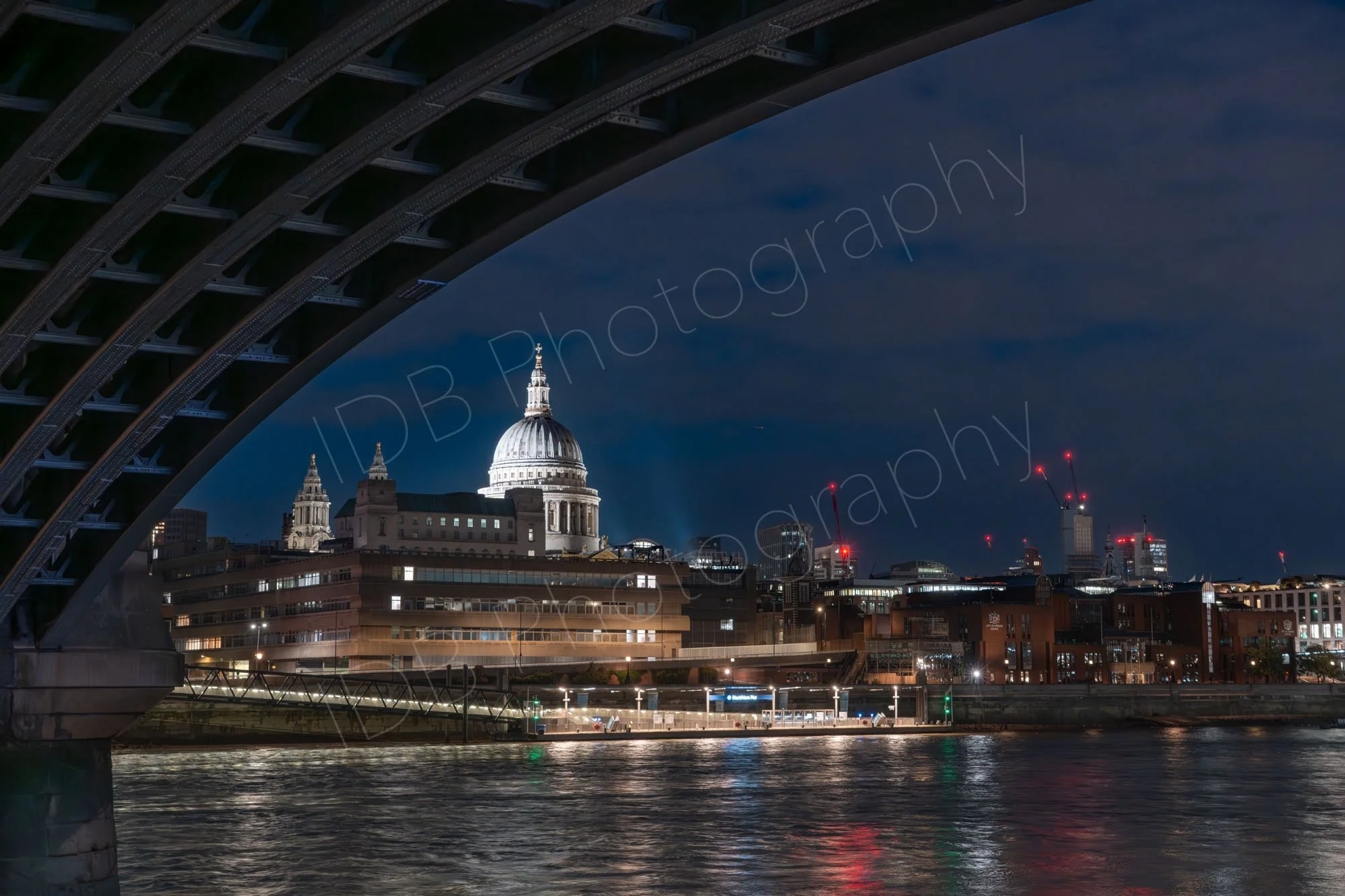 A late evening view of St. Paul's Cathedral framed underneath the structure of Blackfriars Railway Bridge across the River Thames in London.