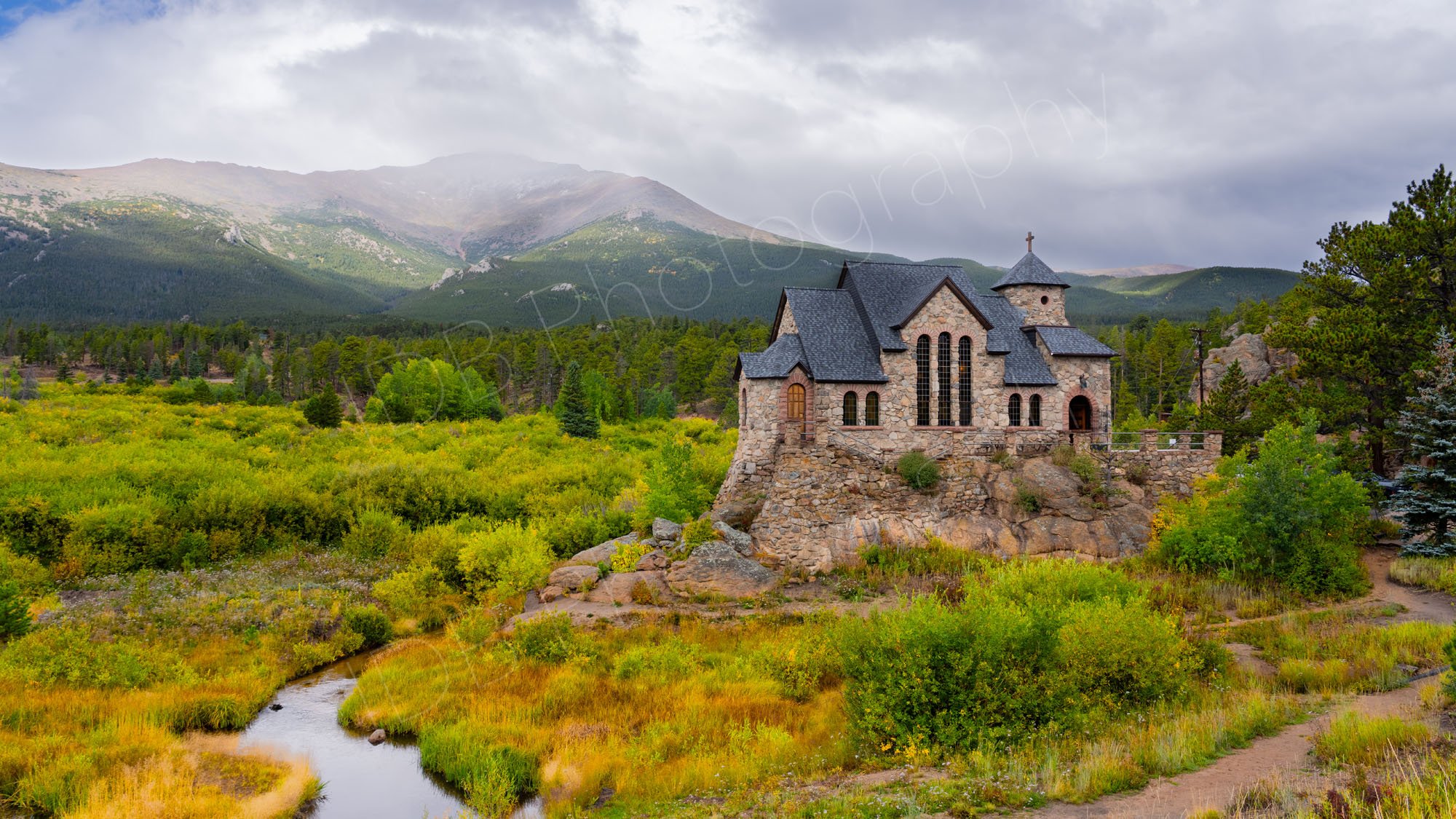 Clouds gathering over the mountains behind the Chapel on the Rock, Colorado with beautiful gold and green foliage in the foreground.