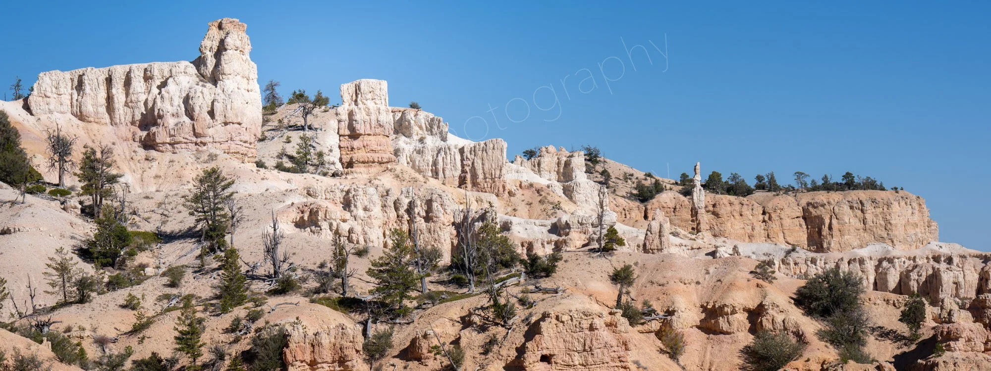 A white and pinky buff desert canyon landscape with tall rock hoodoos at Bryce Canyon National Park in Utah, with blue sky.
