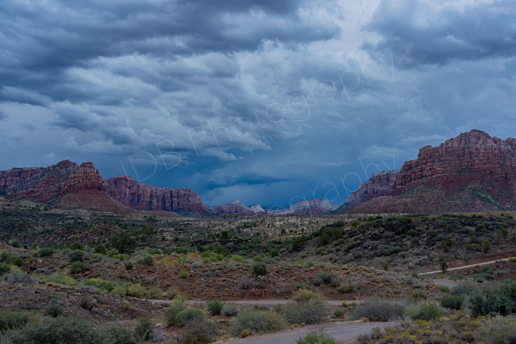 Dramatic Navajo Sandstone cliffs and vast desert landscape of Zion National Park under a heavy, storm-laden sky. 