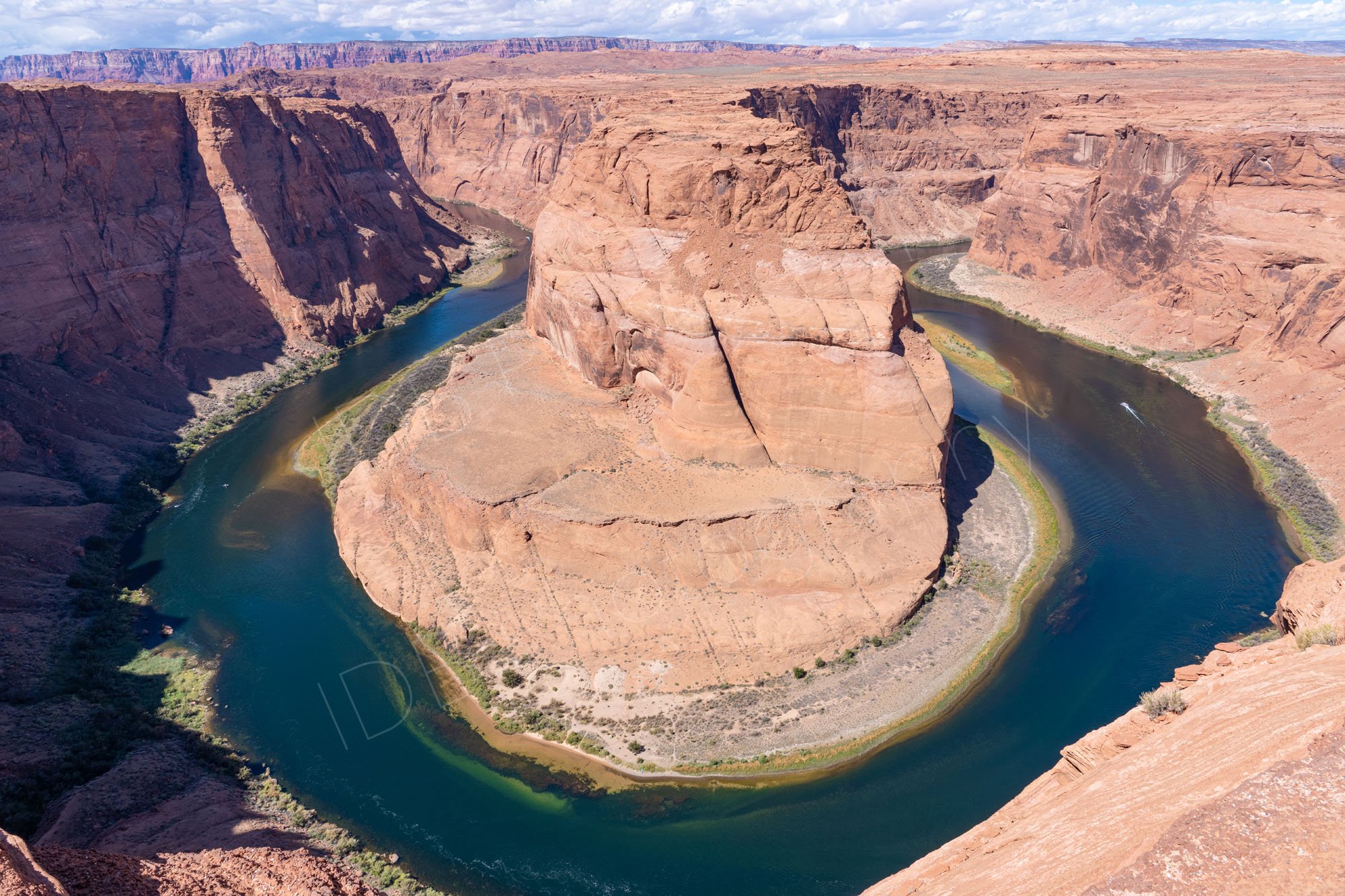 The dramatic Horseshoe Bend on the Colorado River near Page, Arizona, deep blue/green water with red/brown cliffs, clouds in distance.