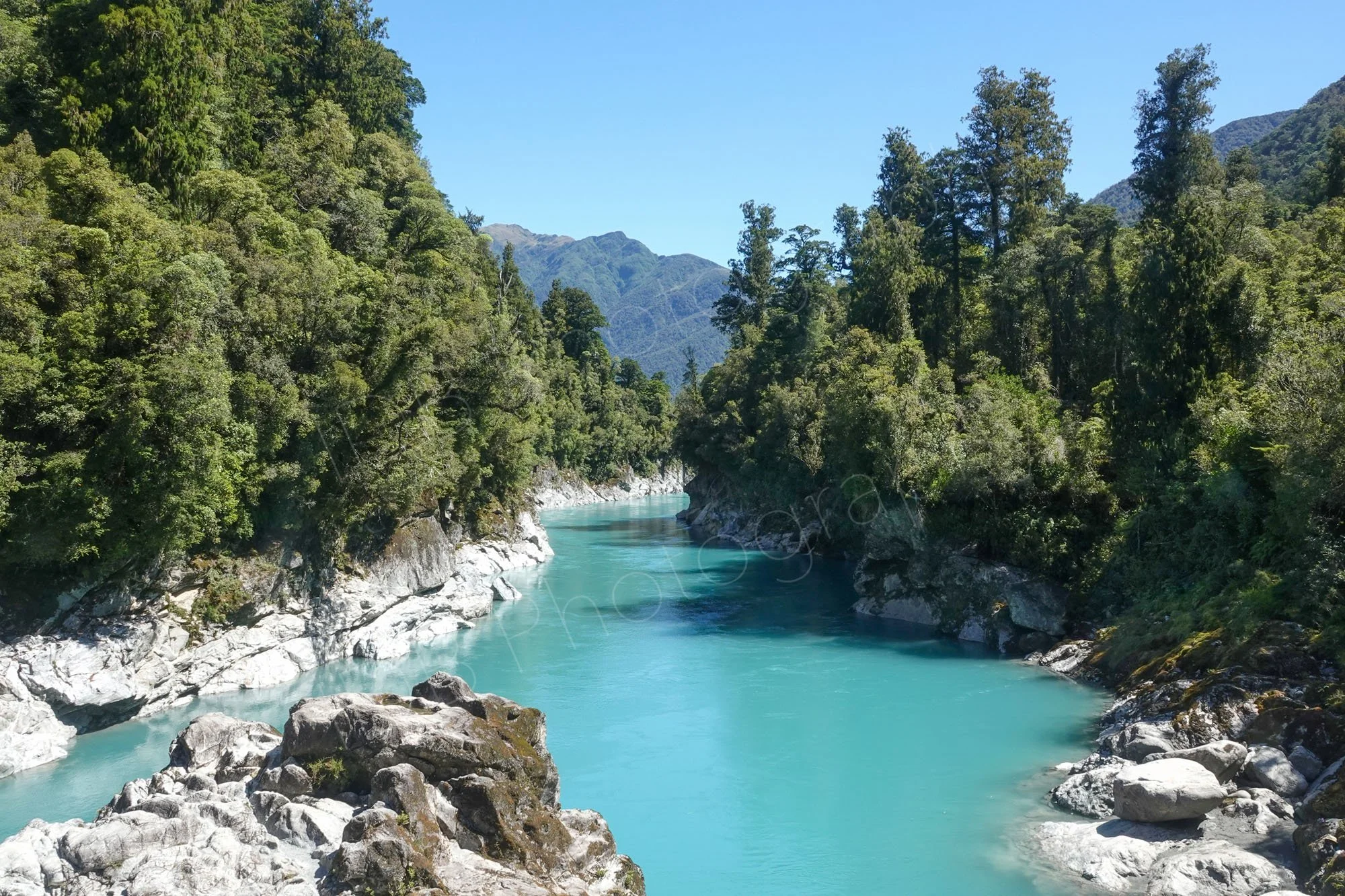 Hokitika Gorge, West Coat, New Zealand, beautiful pale blue water lined by rocks and trees, with blue sky.