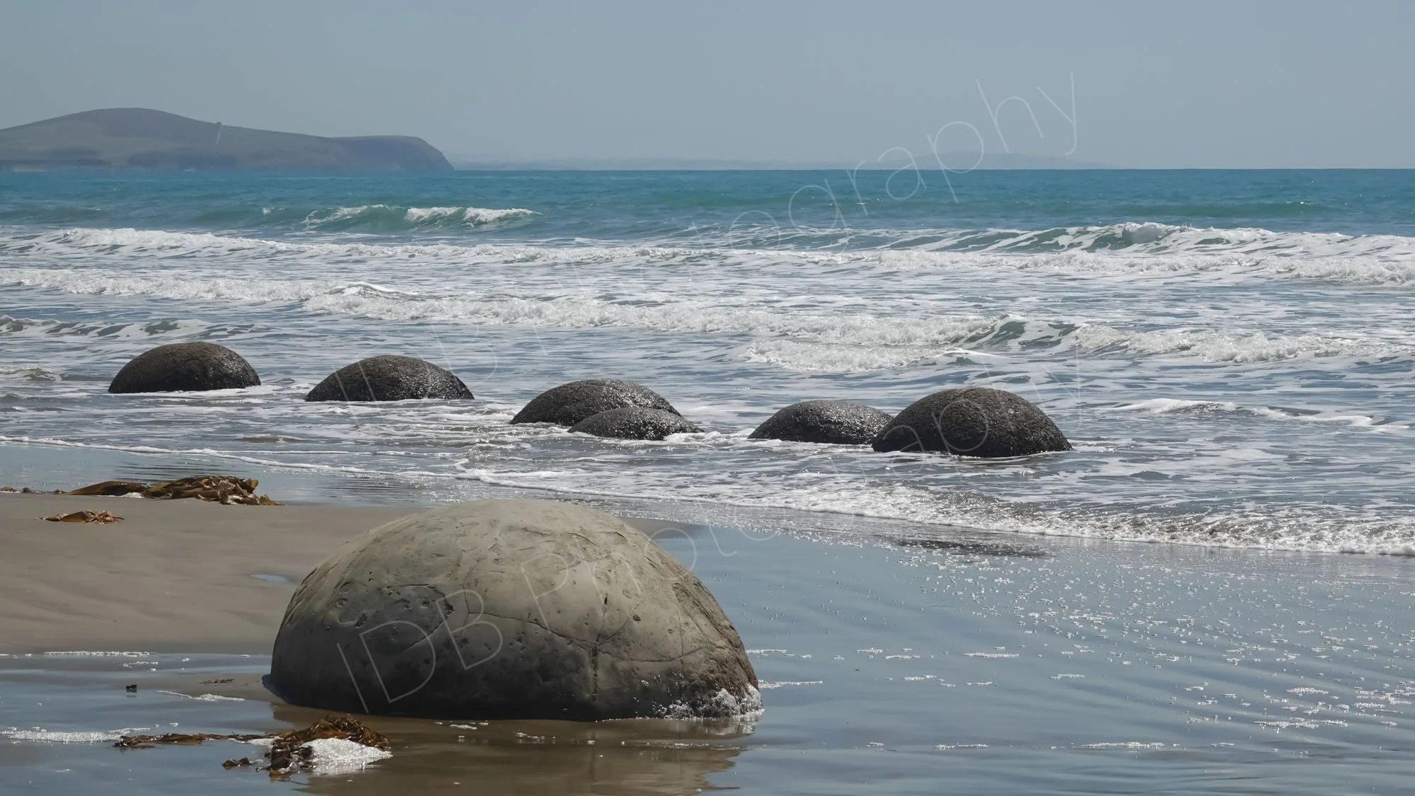Five rounded boulders in the sea with another on the beach in the foreground at Boulder Beach, Otago, New Zealand.