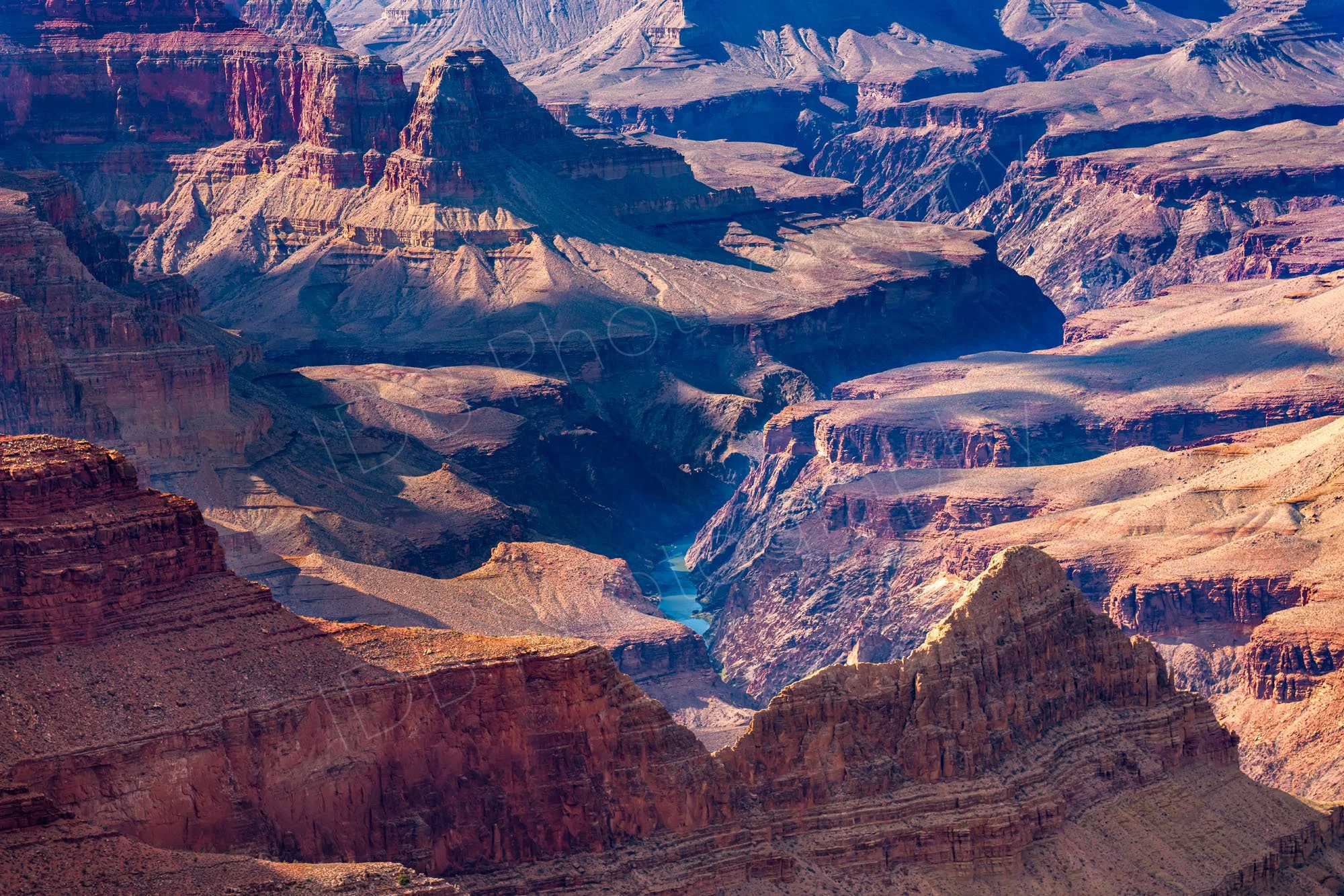 Grand Canyon in Arizona, featuring deep red rock formations and the Colorado River winding through the canyon floor.