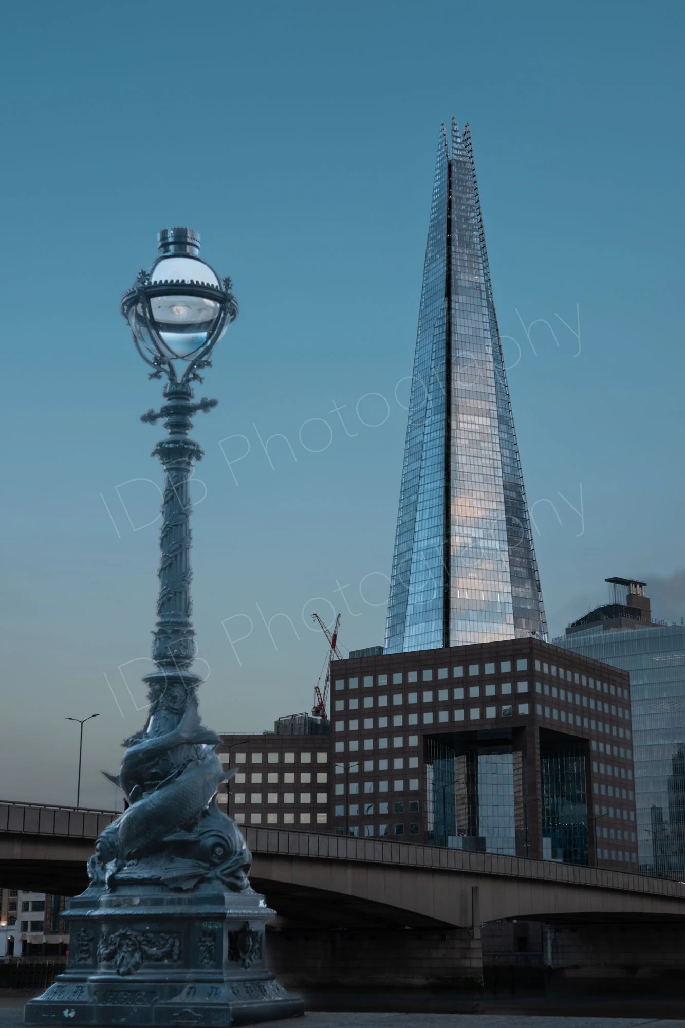An ornate, fish embellished Thames embankment lamppost in the foreground with the iconic skyscraper The Shard rising in the background. 