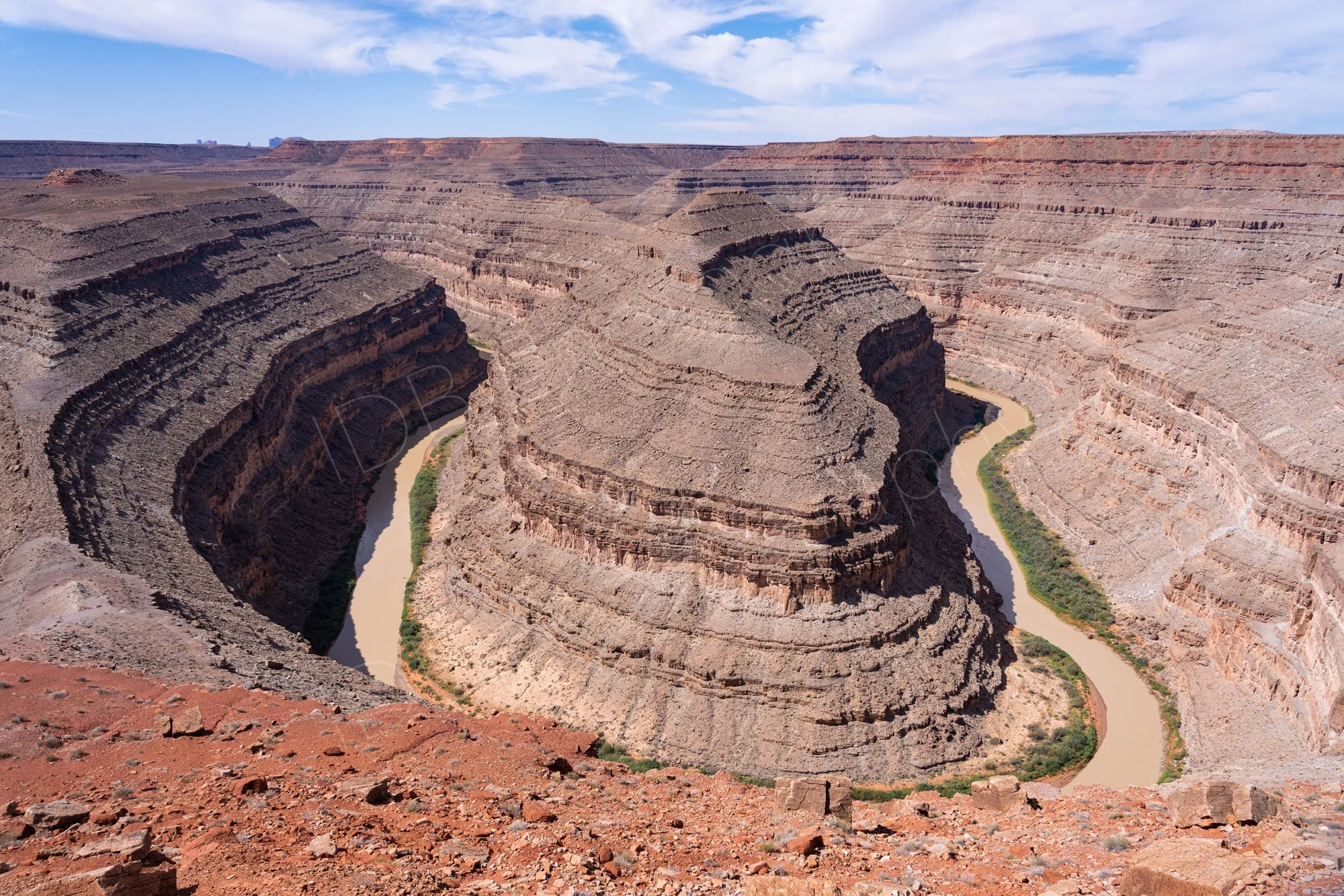 Beautiful stepped and banded cliffs and canyons of the San Juan River meanderings at Goosenecks State Park, Utah; cloudy blue sky.