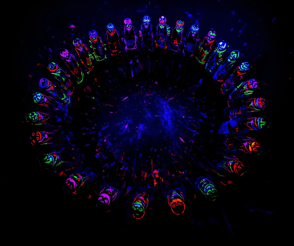Group of people standing in a circle, wearing glow-in-the-dark neon clothing and helmets with LED lights, in dark environment with neon and star-like effects.