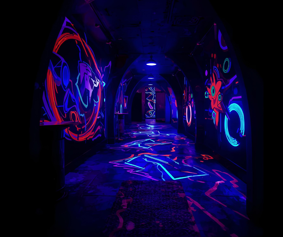 Dark hallway decorated with blacklight-illuminated neon artwork, including Pokémon character Lucario on the left wall and a stylized creature on the right wall, with glowing floor patterns