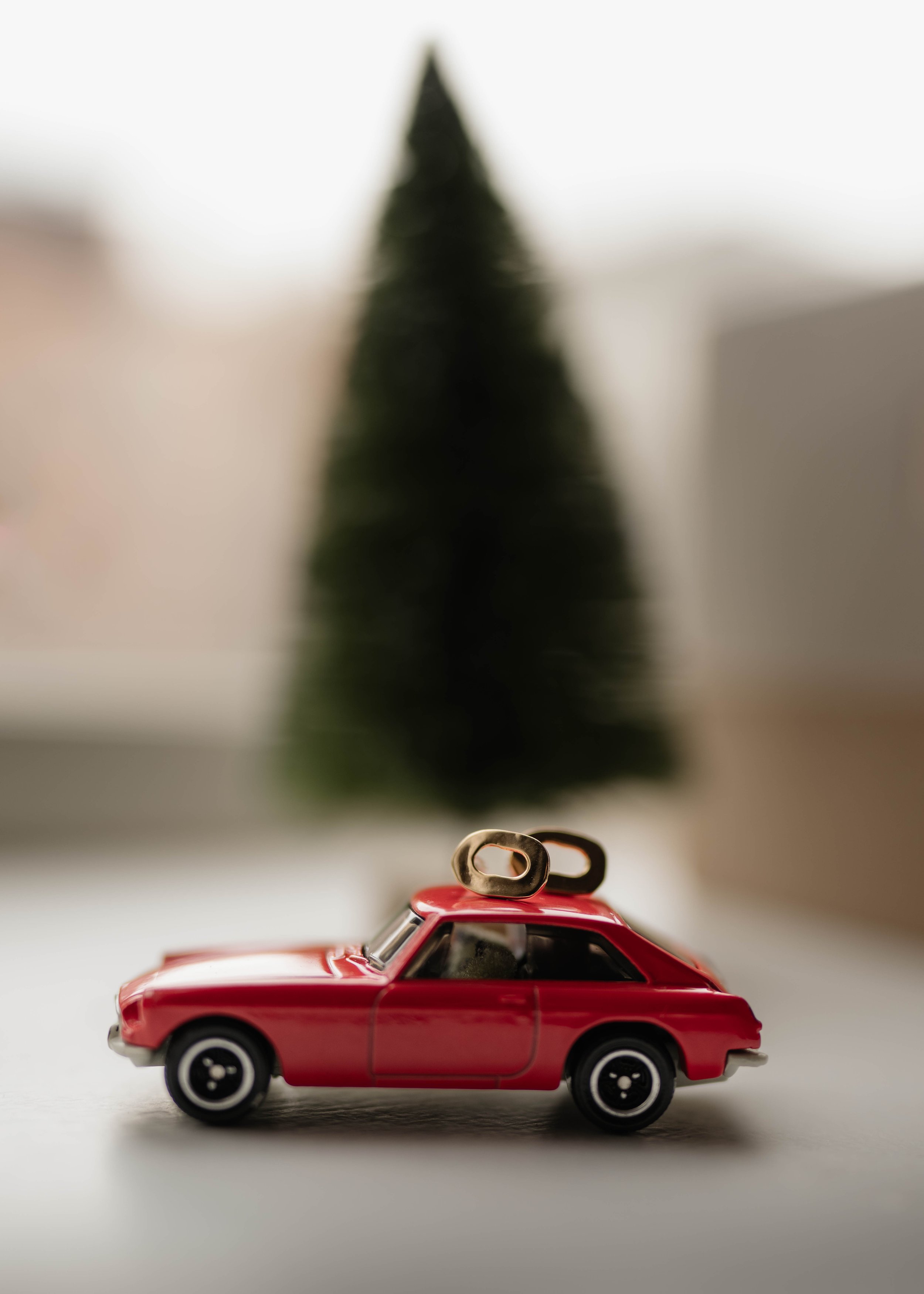 Small red toy car with two bottle openers on top, in front of a blurred background of a Christmas tree.