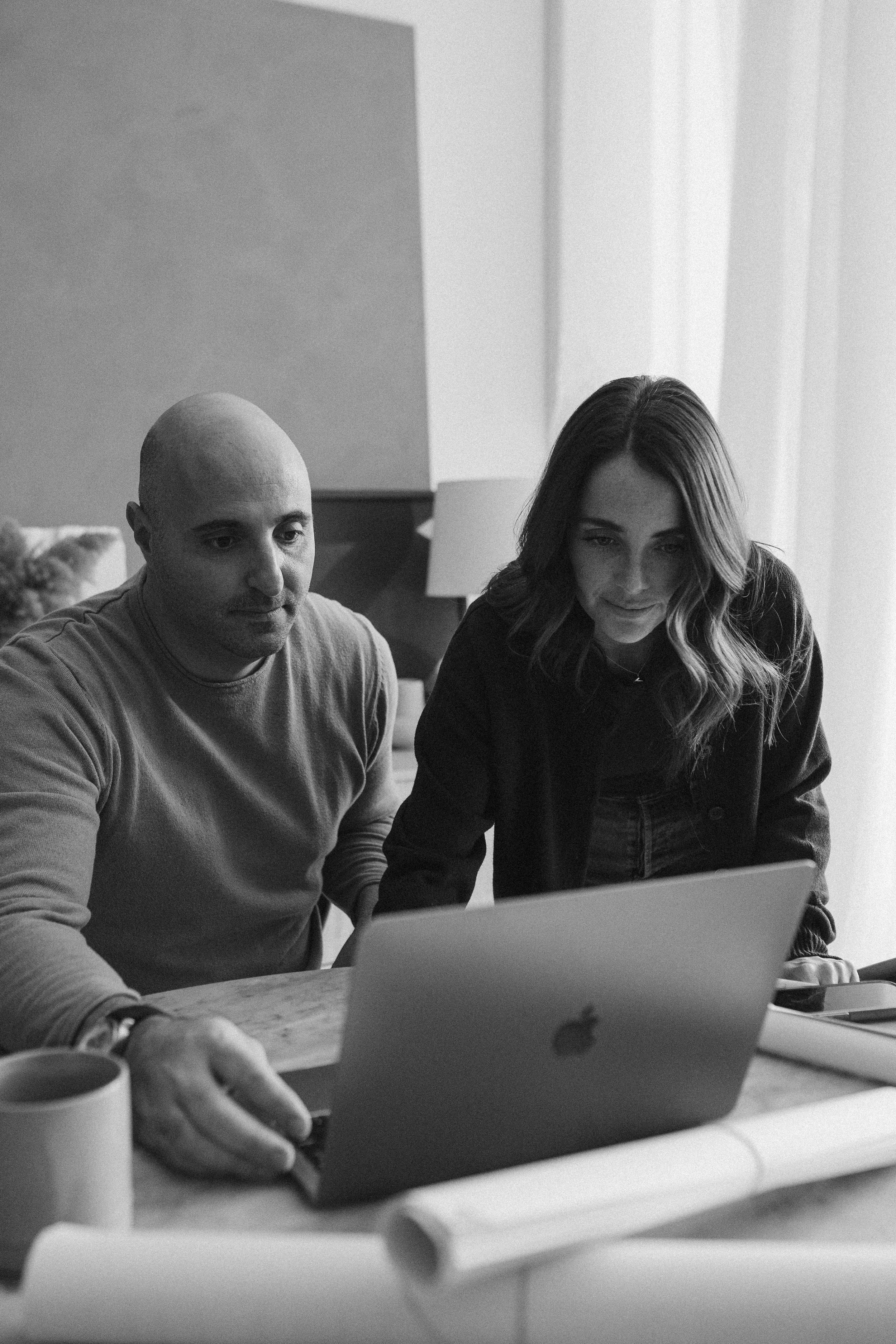A man and a woman looking at a laptop screen together at a table in a room.