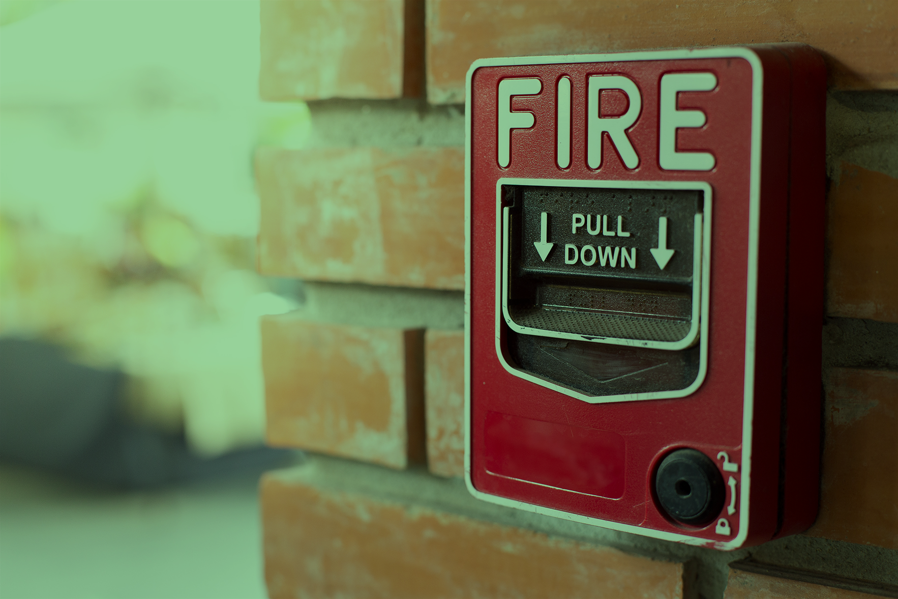 Red fire alarm pull station mounted on a brick wall.