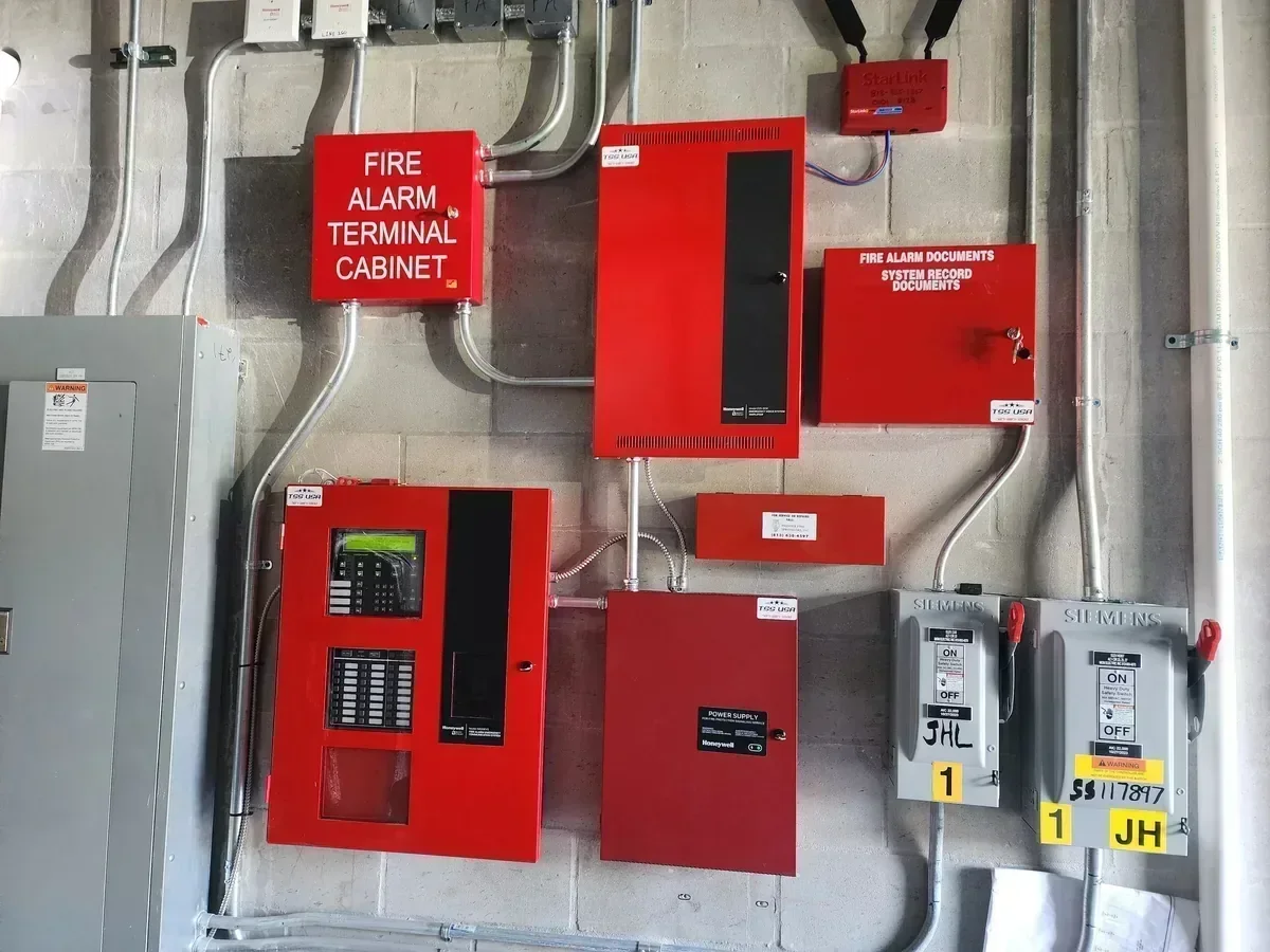 Fire alarm system with control panel, alarm cabinet, and related devices mounted on a concrete wall.