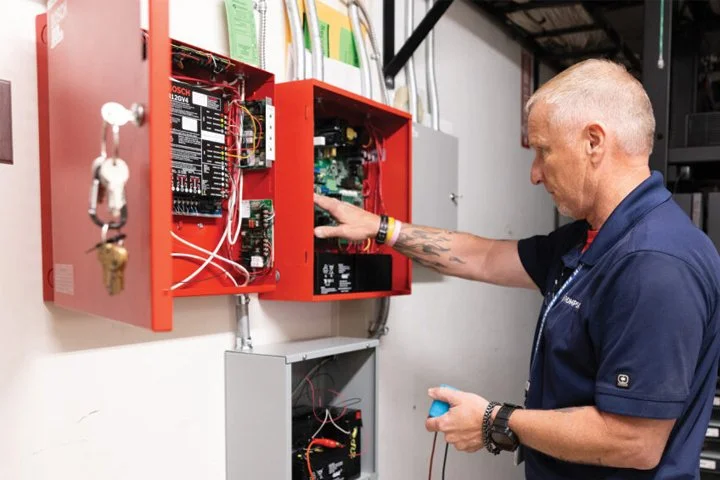A technician working on an electrical control panel in a workshop or electrical room.
