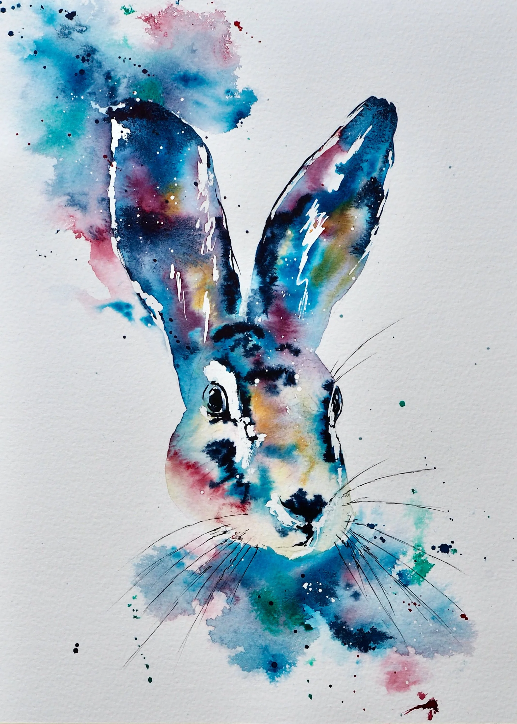 Watercolor painting of a rabbit's face with large ears, using splashes of blue, pink, yellow, and green ink on white paper.