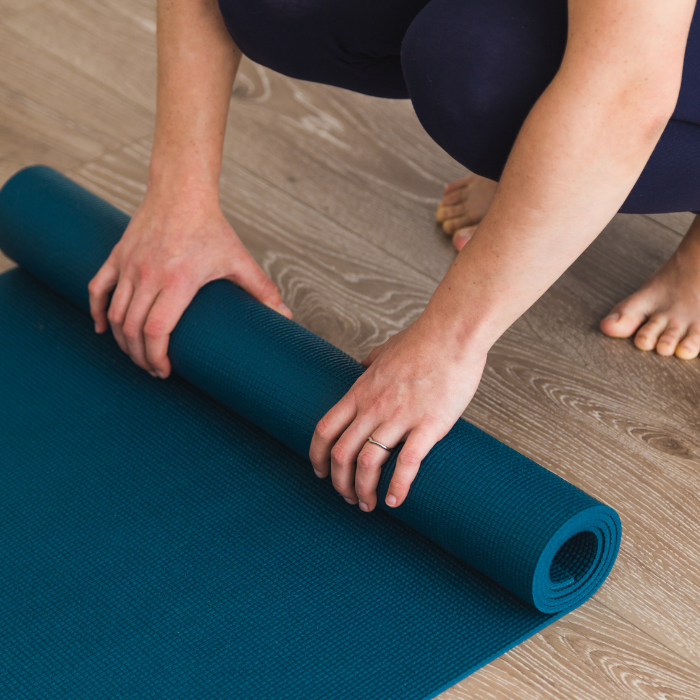 Person rolling out a blue yoga mat on wooden floor.