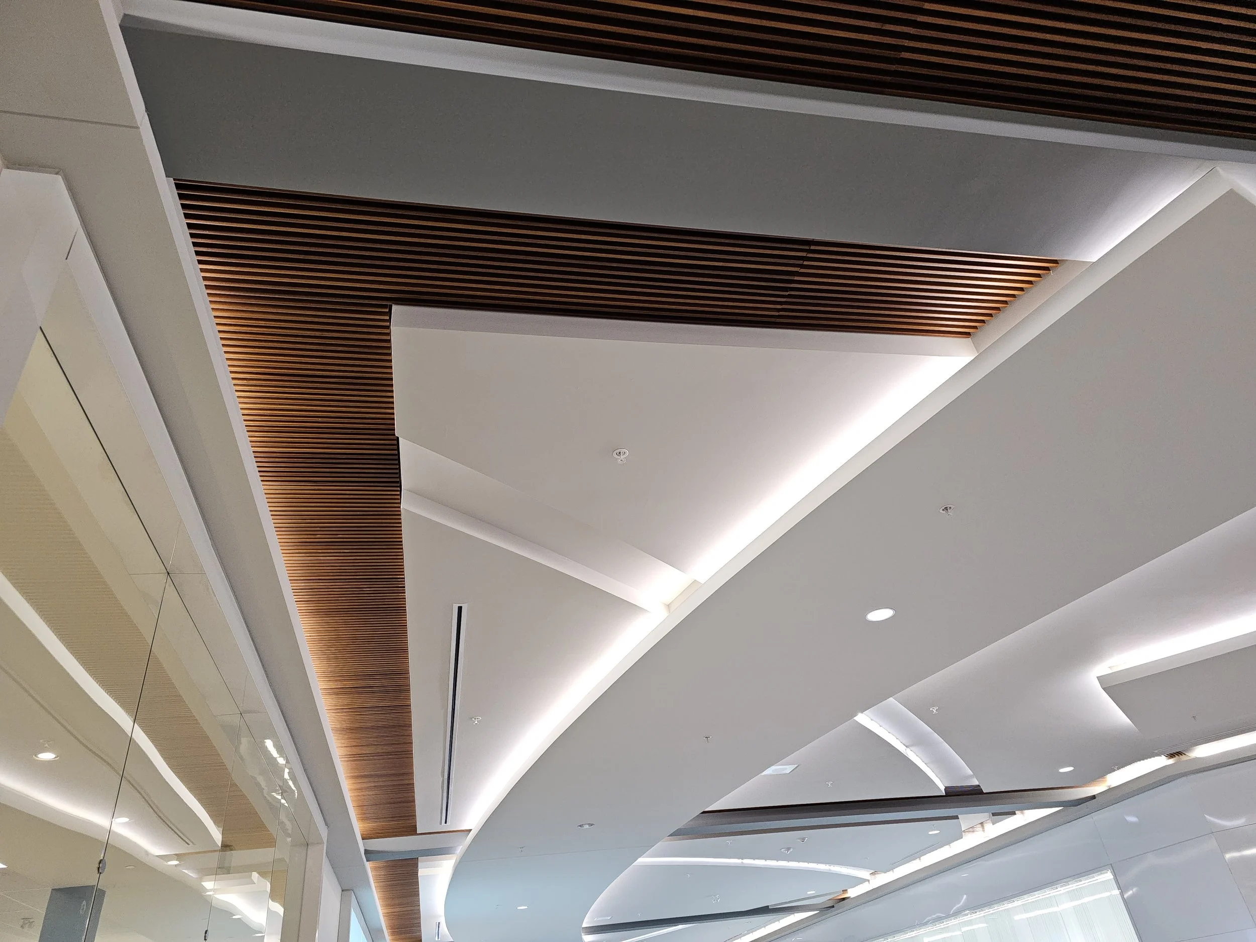 Ceiling design in a modern building with curved white surfaces, wooden slats, and concealed lighting.