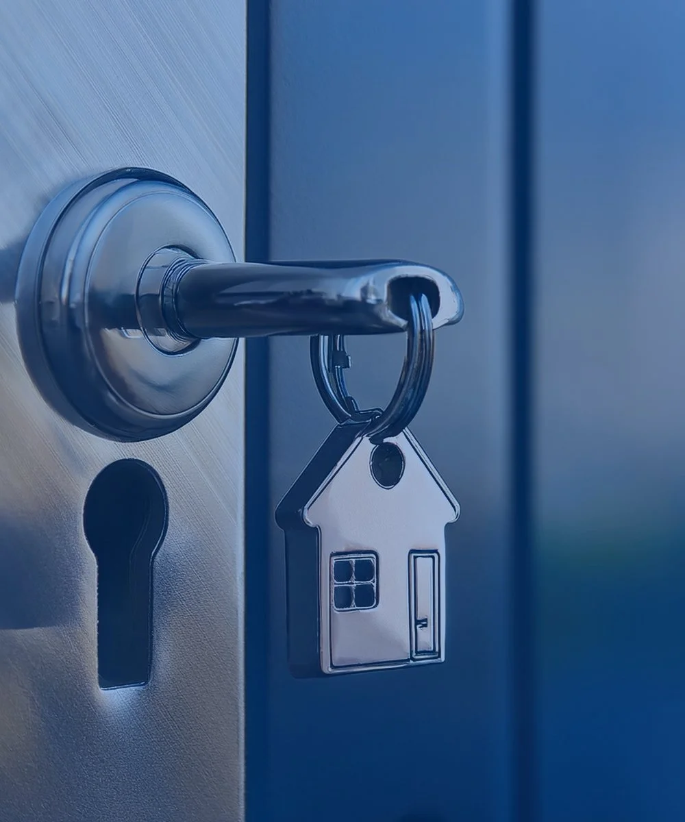 Key with house-shaped keychain hanging in lock on a metal door.