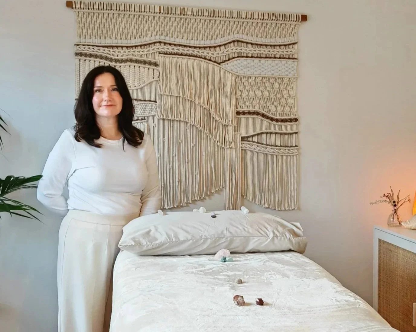 Jill from Divine Reiki standing with the massage bed, infront of tapestry.