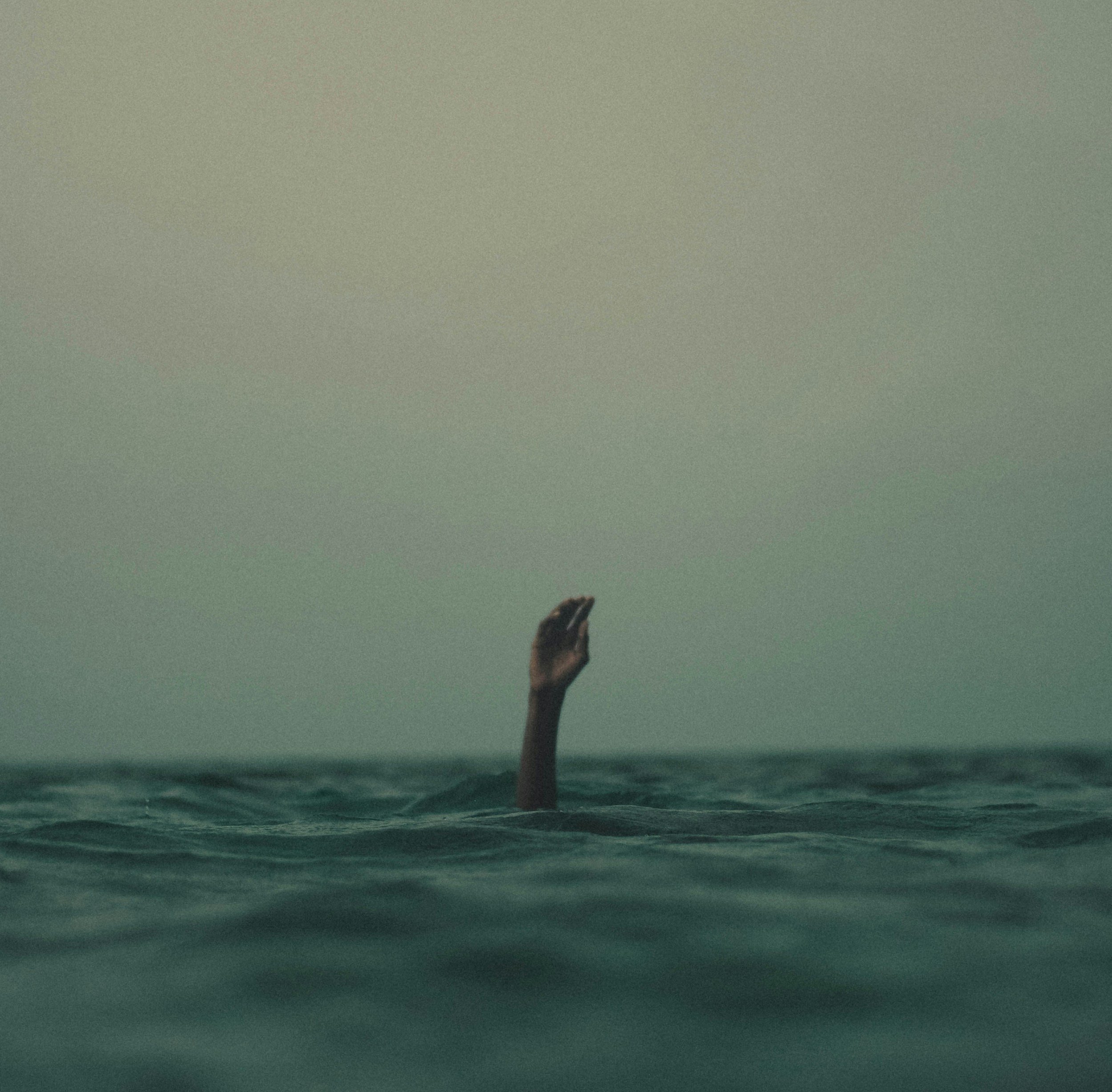 A person submerged in water up to their head, with only one hand and part of the arm visible above the surface.