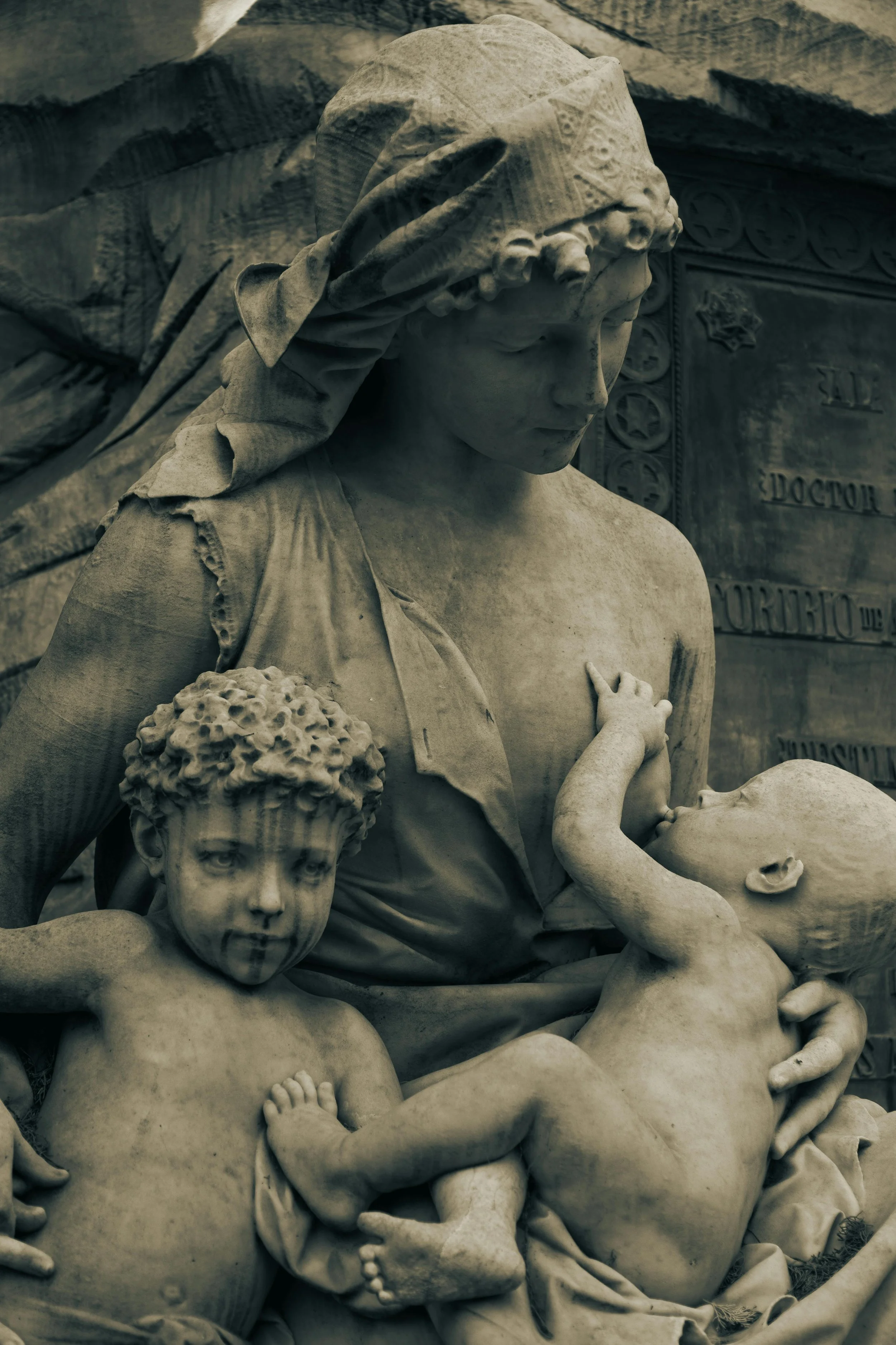 Marble sculpture depicting a tender scene of a woman with two children, breastfeeding the infant.