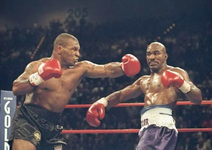 Mike tyson et Holyfield en plein combat dans un ring, l'un donnant un coup de poing à l'autre qui tente de se défendre.
