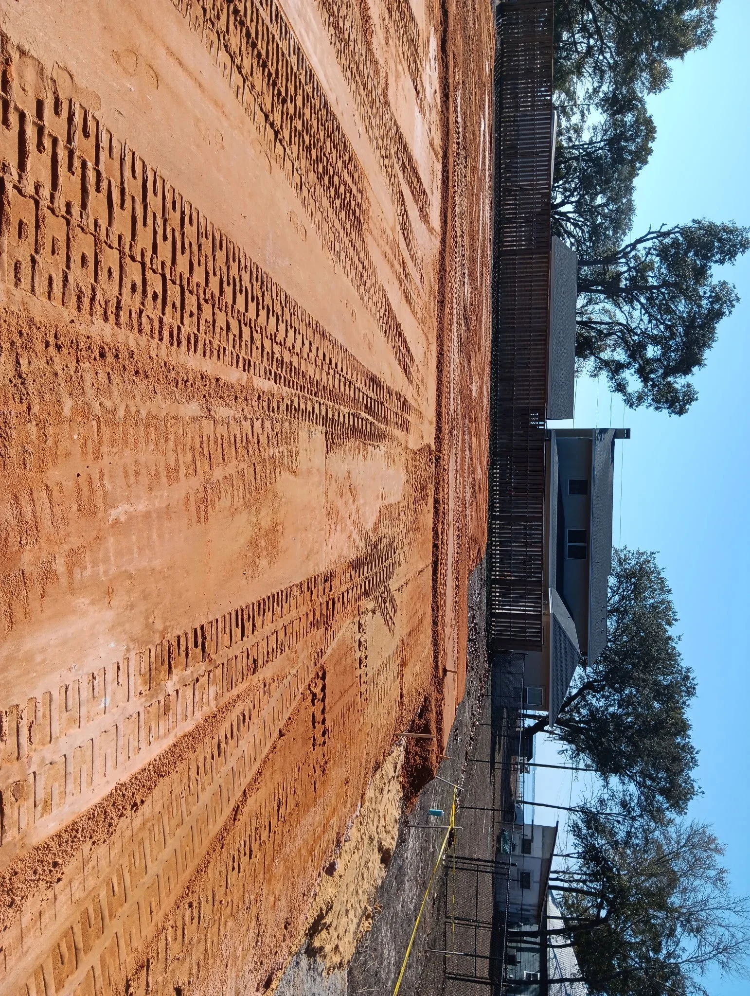 Construction site with freshly laid red brick pavement and a residential house in the background, surrounded by trees.