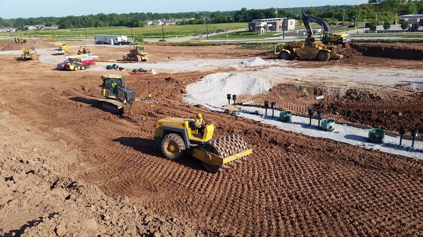 Construction site with heavy machinery, including a roller, excavator, and bulldozers, preparing the ground for building.