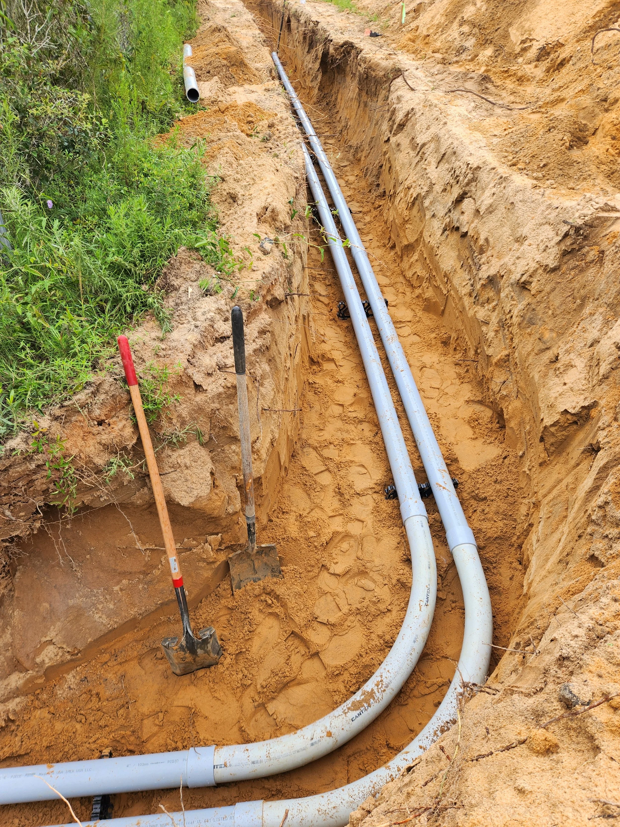 Installation of underground utility pipes in a trench with shovels and construction tools nearby.