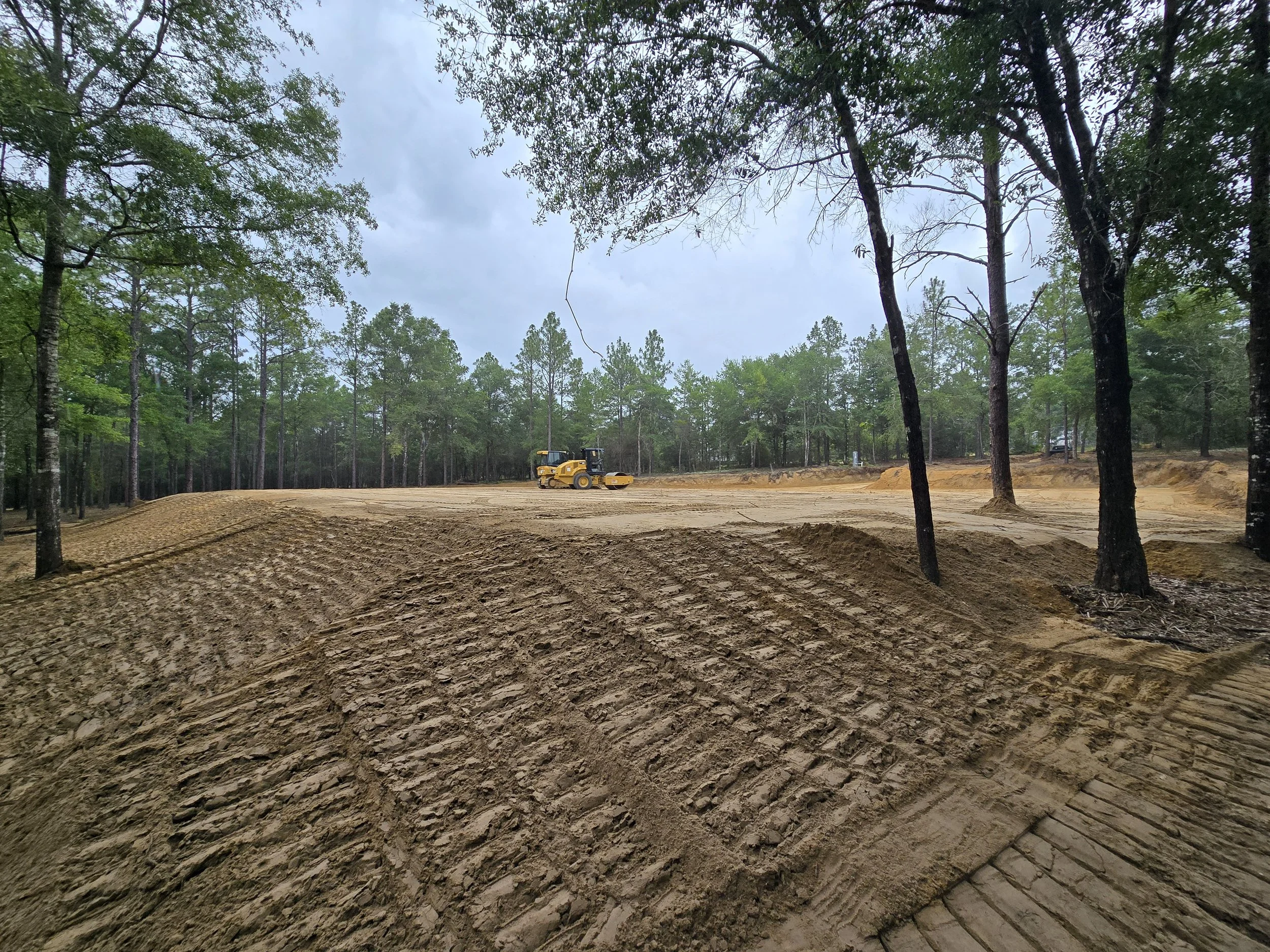 Construction site in a forest with a yellow bulldozer operating on cleared land.