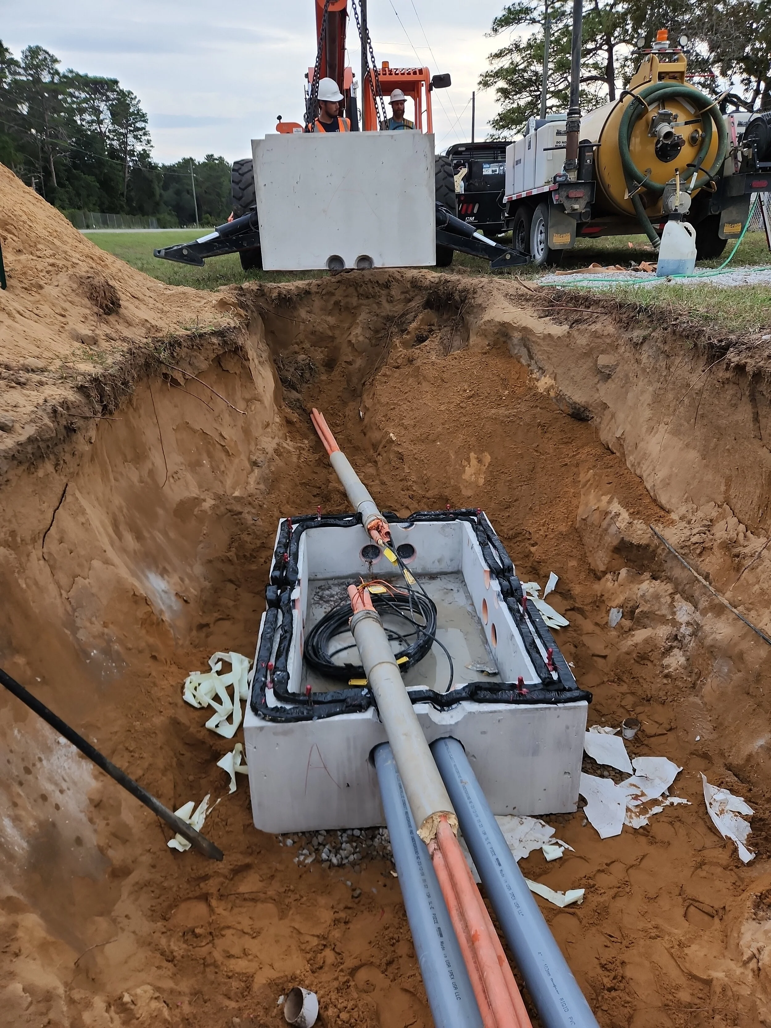 Construction workers installing underground utility lines using large pipes and machinery at a construction site.