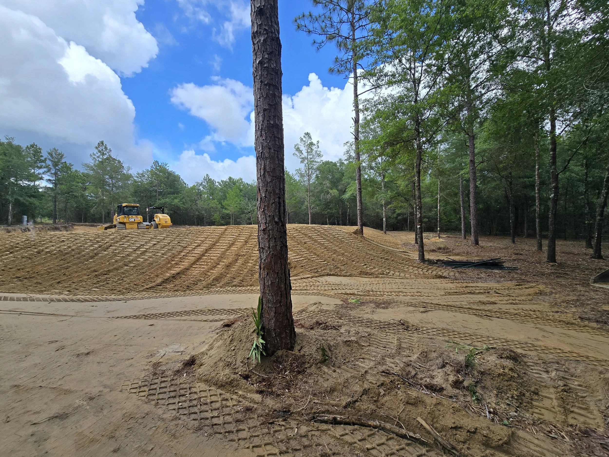 Construction site with bulldozer working on leveling the ground in a forested area under a partly cloudy sky.