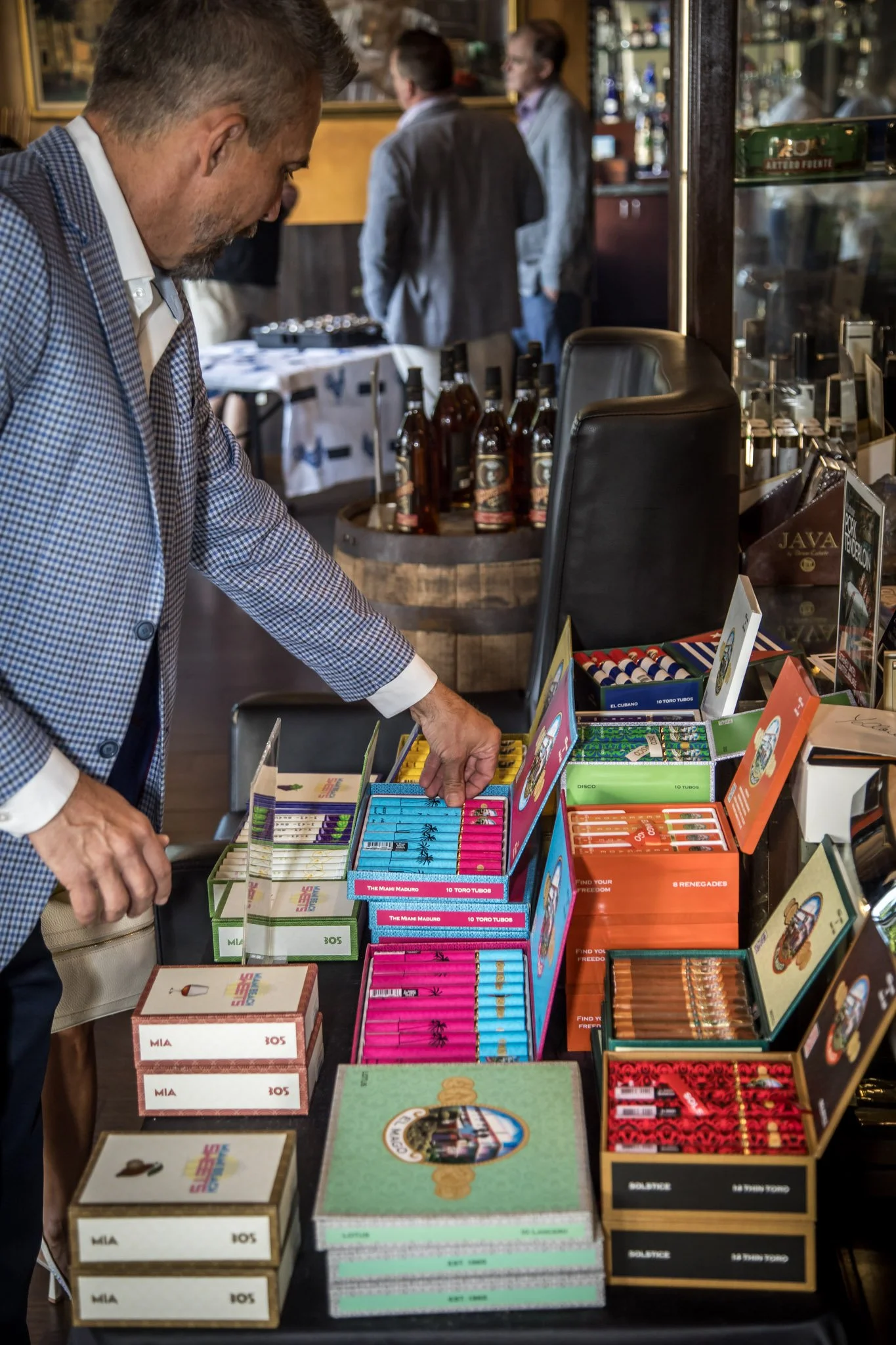 Man shopping for cigars at a store display, with various colorful cigar boxes and packs on the table.
