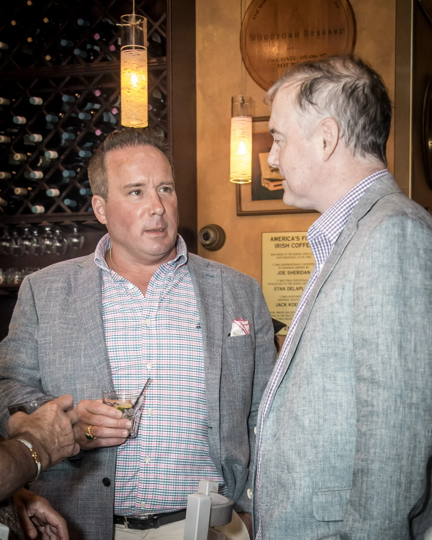 Two men in suits having a conversation at a social event in a restaurant or bar setting.