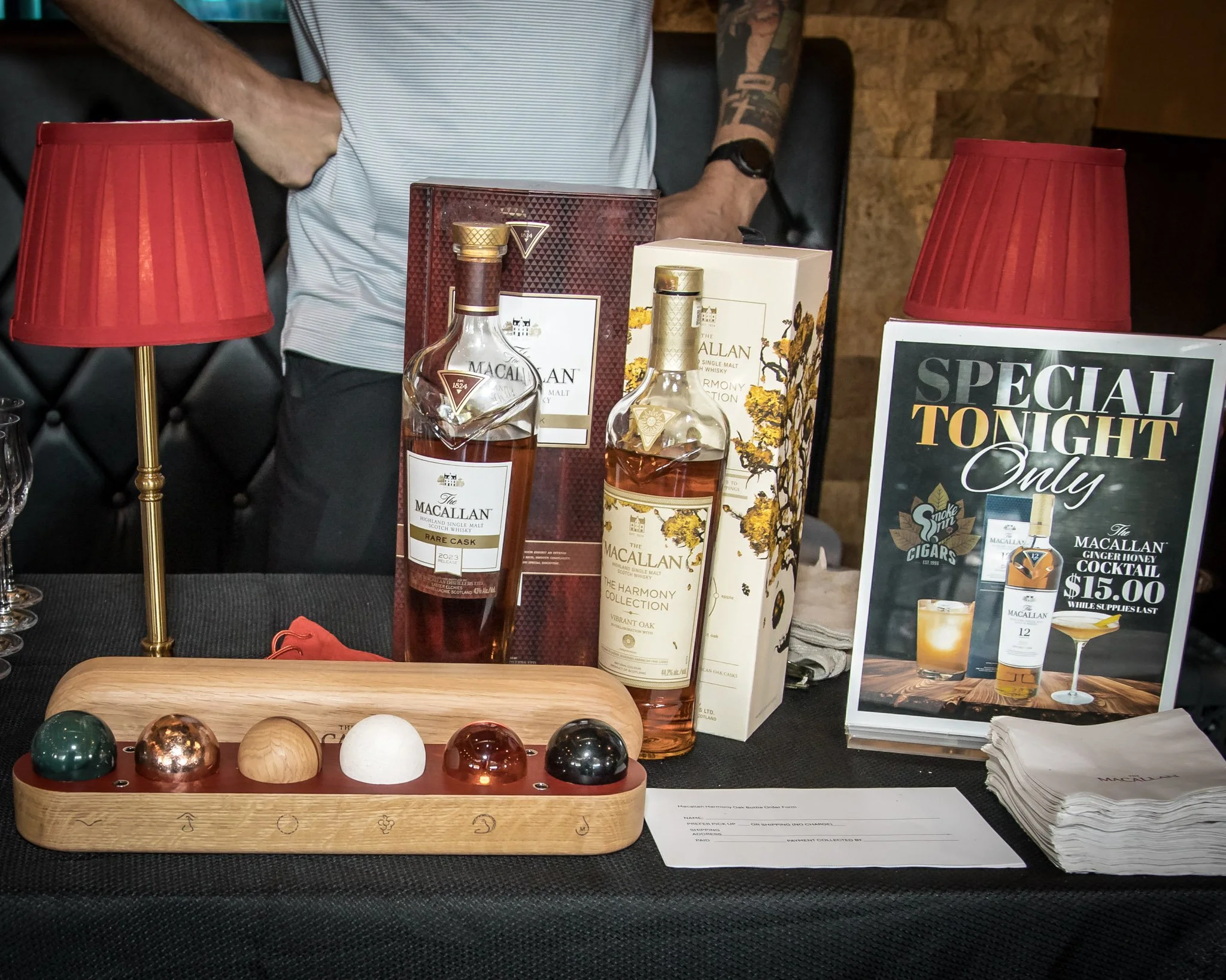 Display of bottle of Macallan whiskey, promotional sign for whiskey cocktails priced at $15.00, and a wooden tray with marble balls.