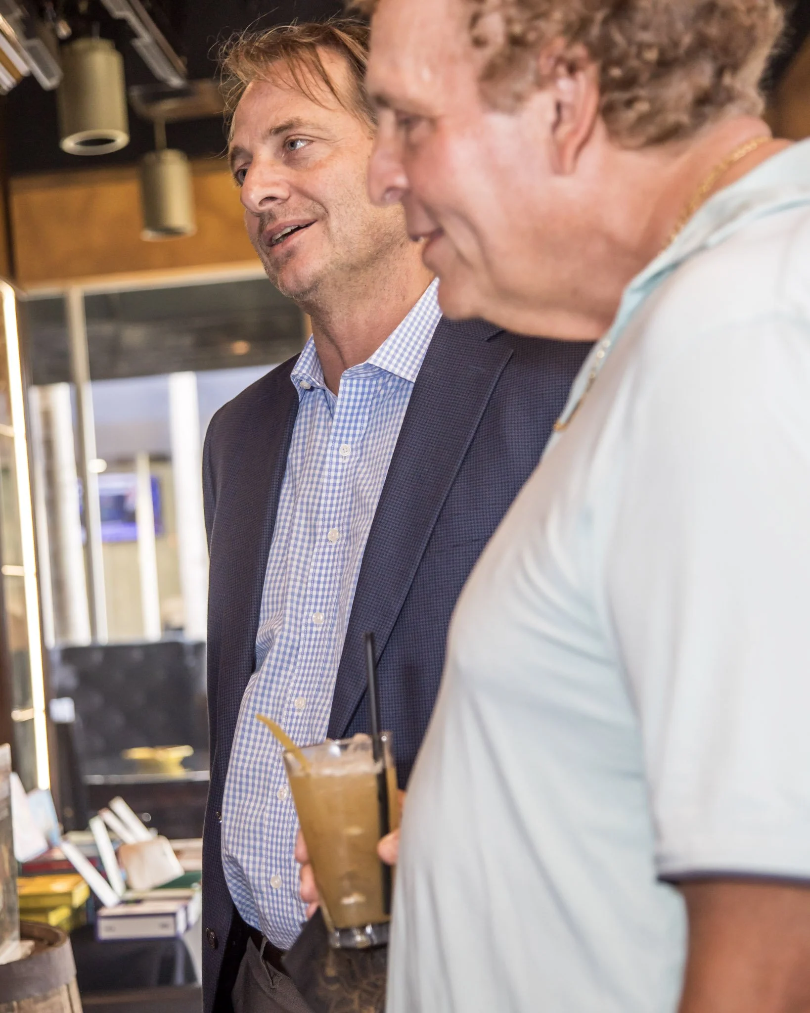 Two men speaking in a bar or restaurant, one with a drink in hand.