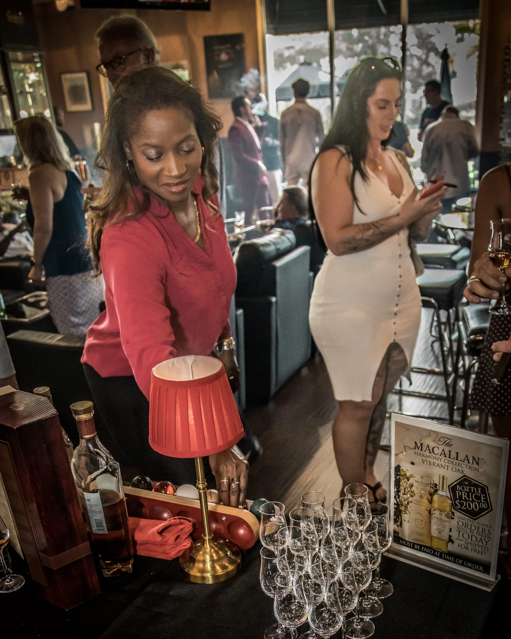 A woman in a red top reaches for an ornament on a table at a gathering in a cozy, dimly lit restaurant.