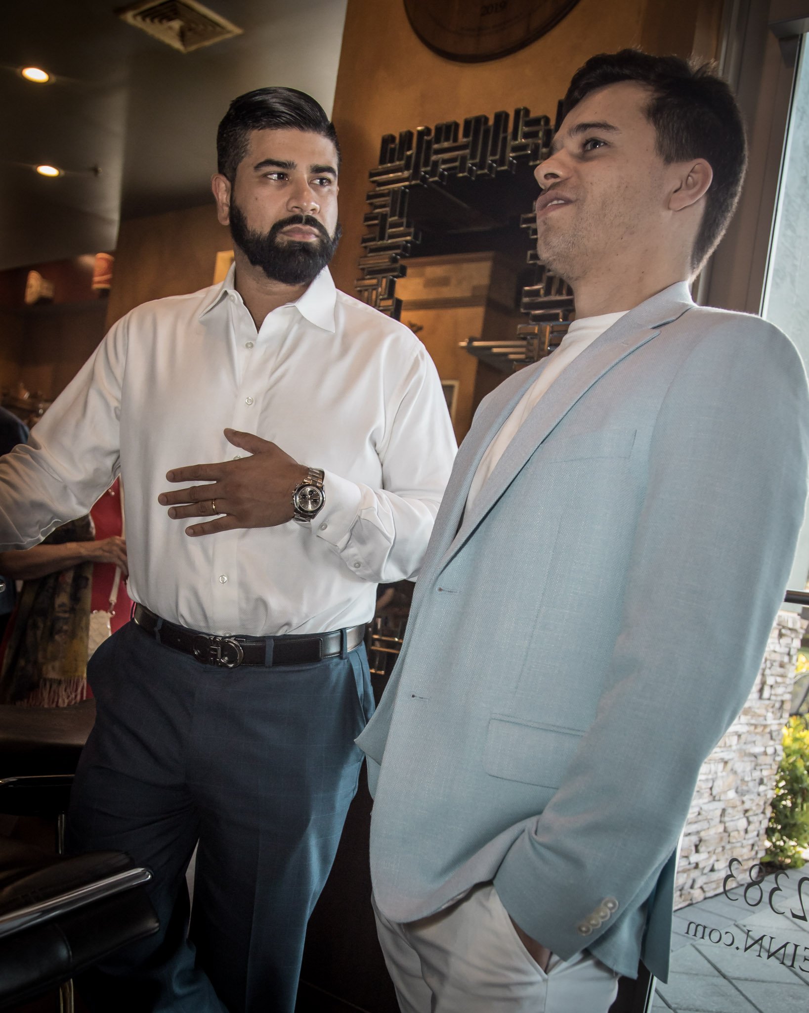 Two men in formal attire having a discussion indoors near a window.
