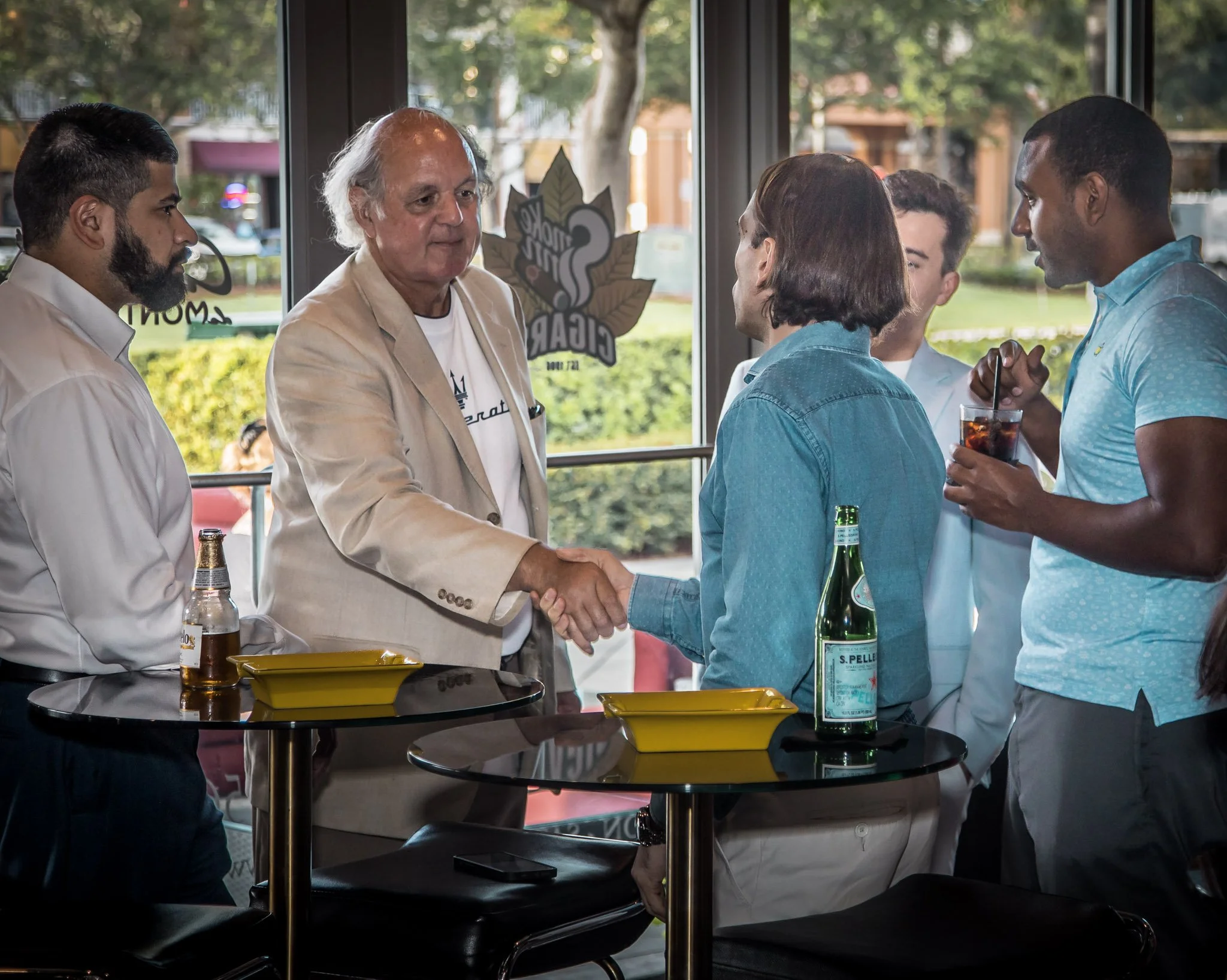 Group of five people a man and woman shaking hands at a social gathering in a restaurant or cafe, with drinks and flyers on the tables.