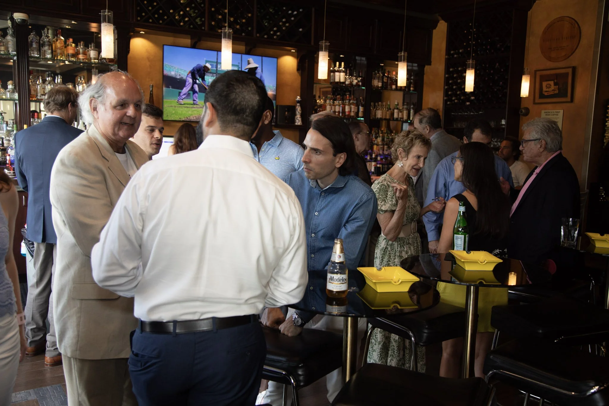 People socializing at a bar or restaurant, engaged in conversation, with a TV screen displaying a golf game in the background.