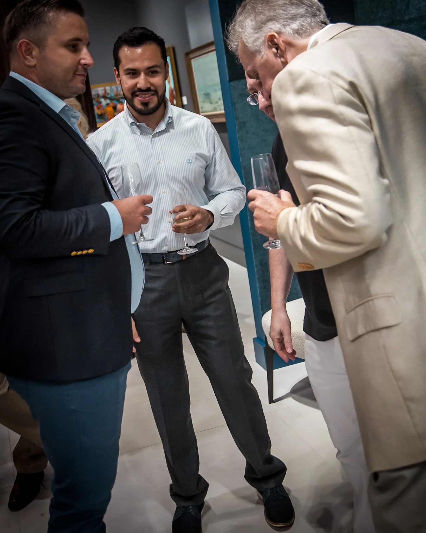 Group of four men in business attire having a conversation at a social gathering, holding champagne glasses.