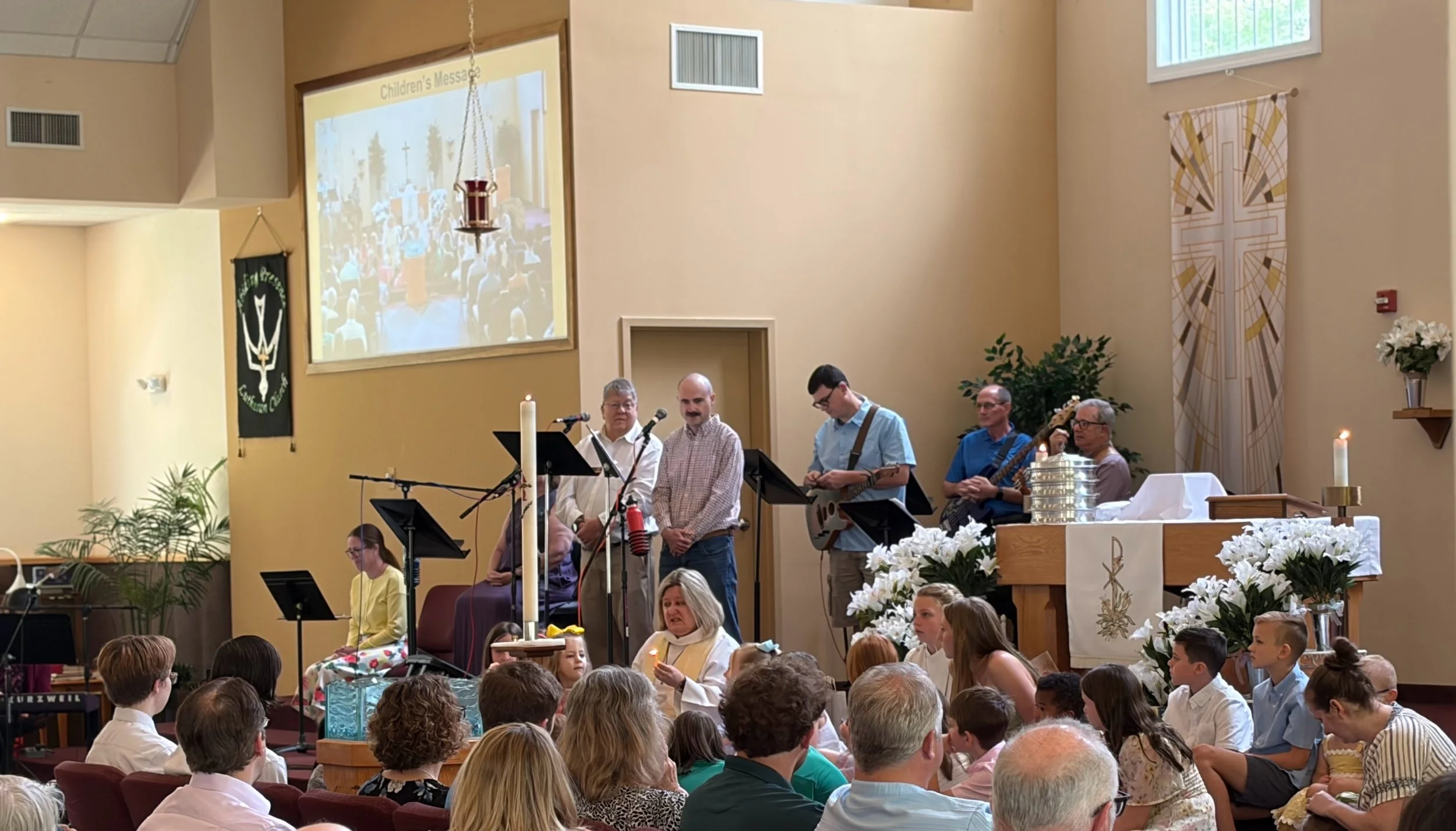 Pastor Kim sitting with the children on Easter giving the children's message while the Praise Band looks on from the back.